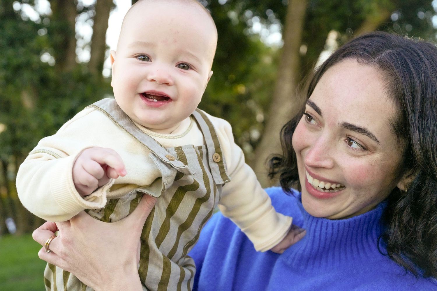 A joyful outdoor moment captured with a baby wearing stripes and a blue sweater.
