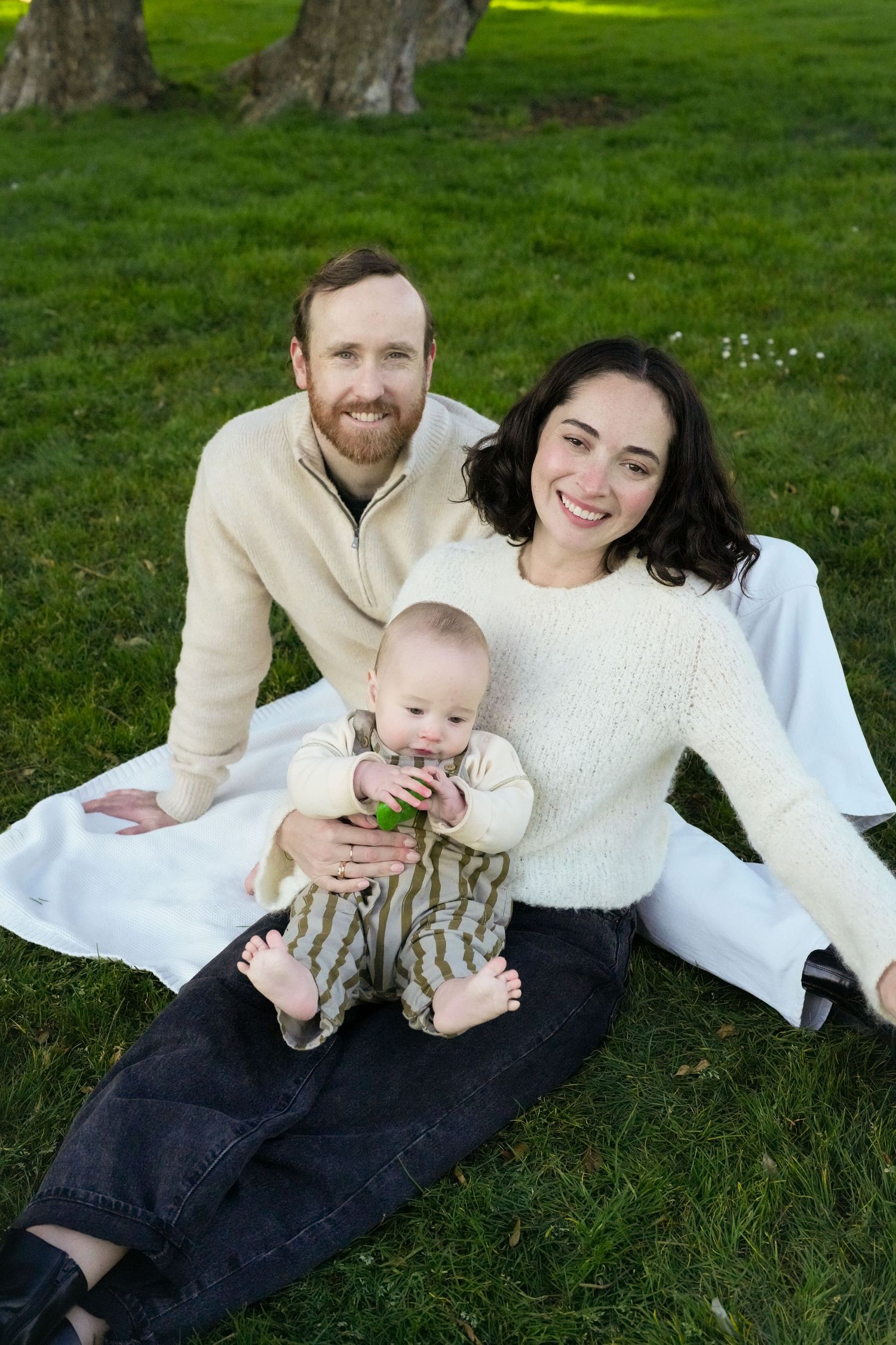 Family relaxing together on grass with baby on sunny afternoon.