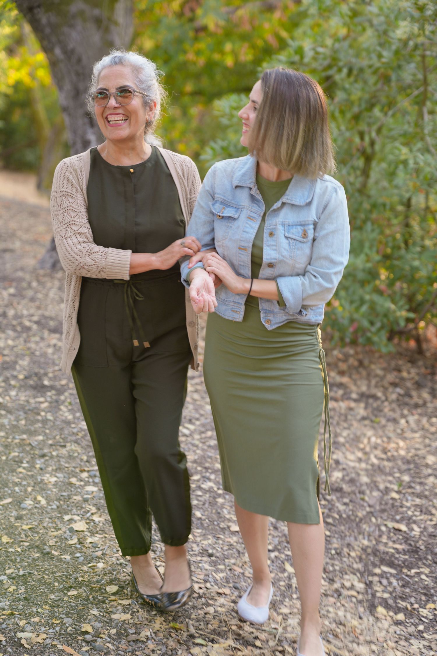 Two people share candid moments together on a path surrounded by autumn foliage.