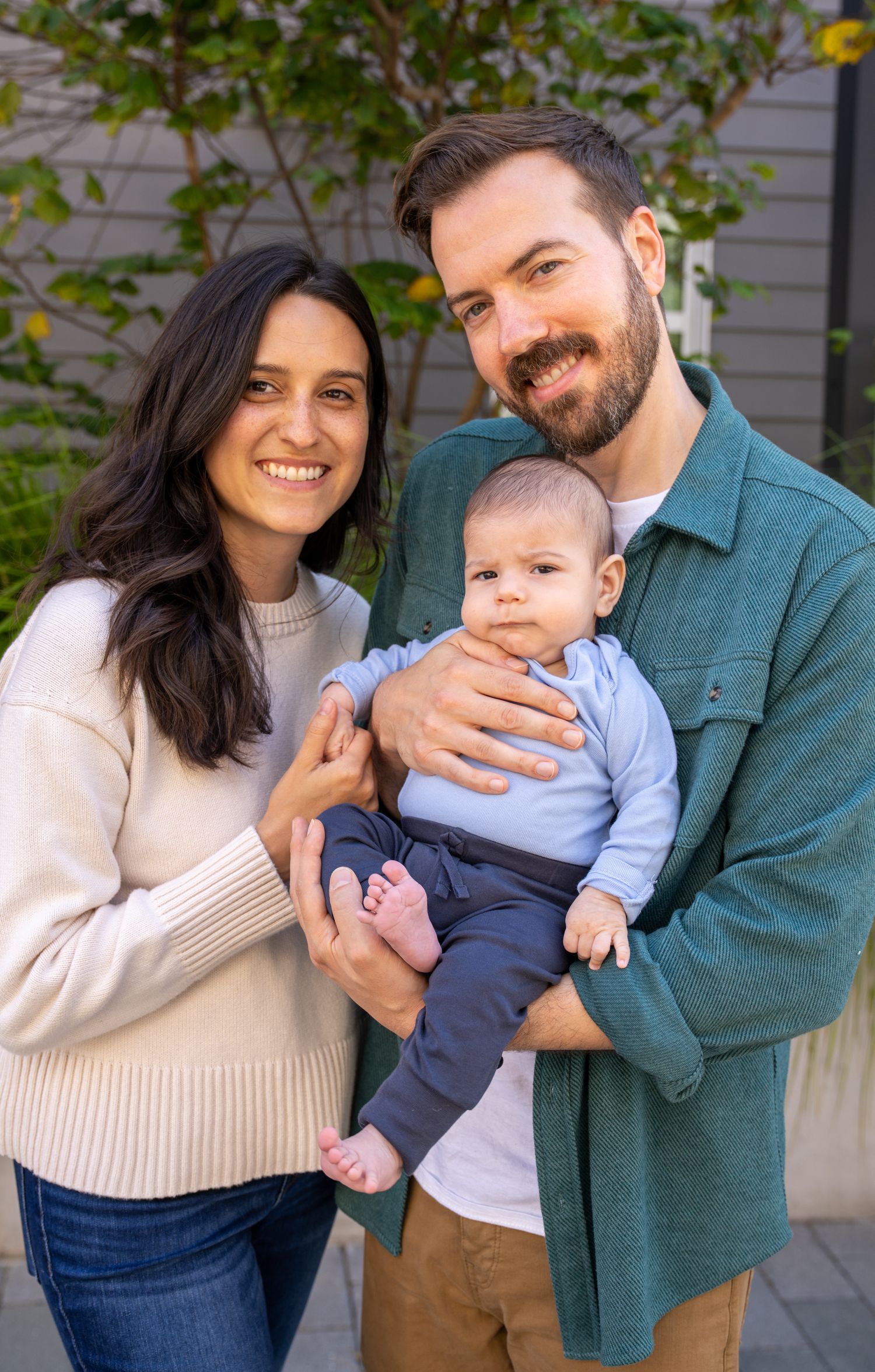 A happy family of three poses together outdoors in casual fall attire for a series of candid portrait photos.