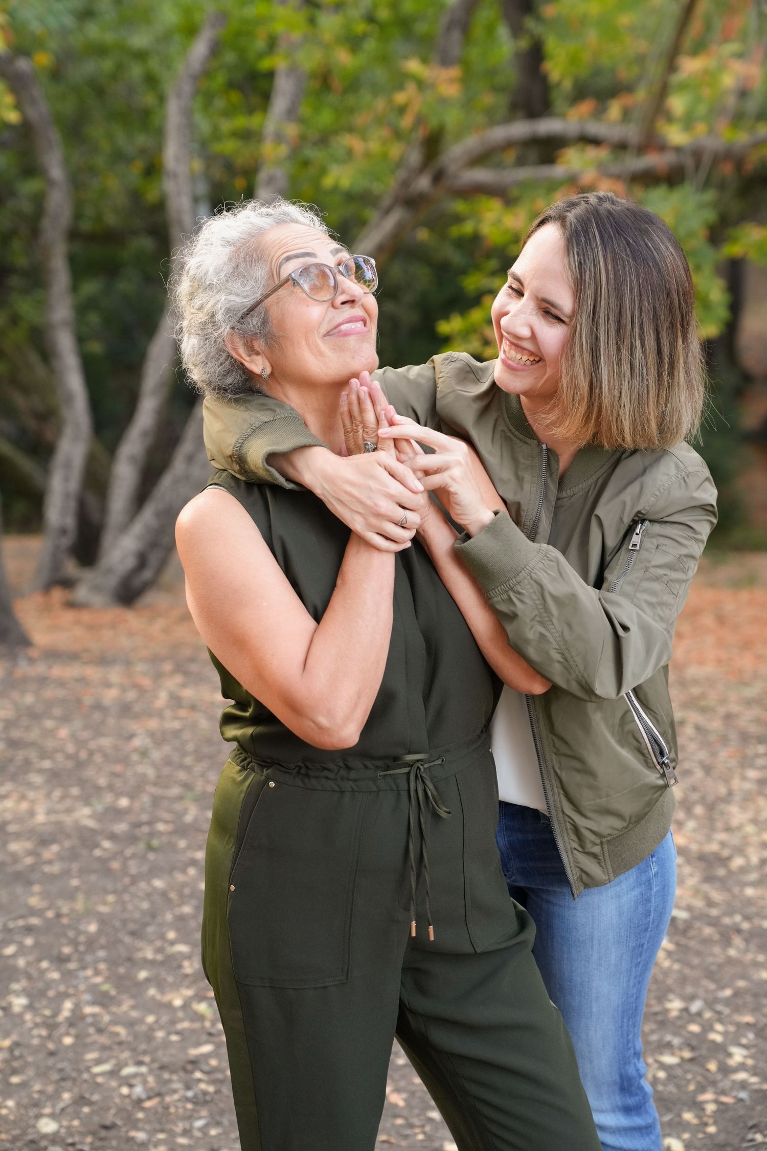 Two people share a joyful moment hugging and laughing together in a park. It's summer in California so there are fallen bay leaves.