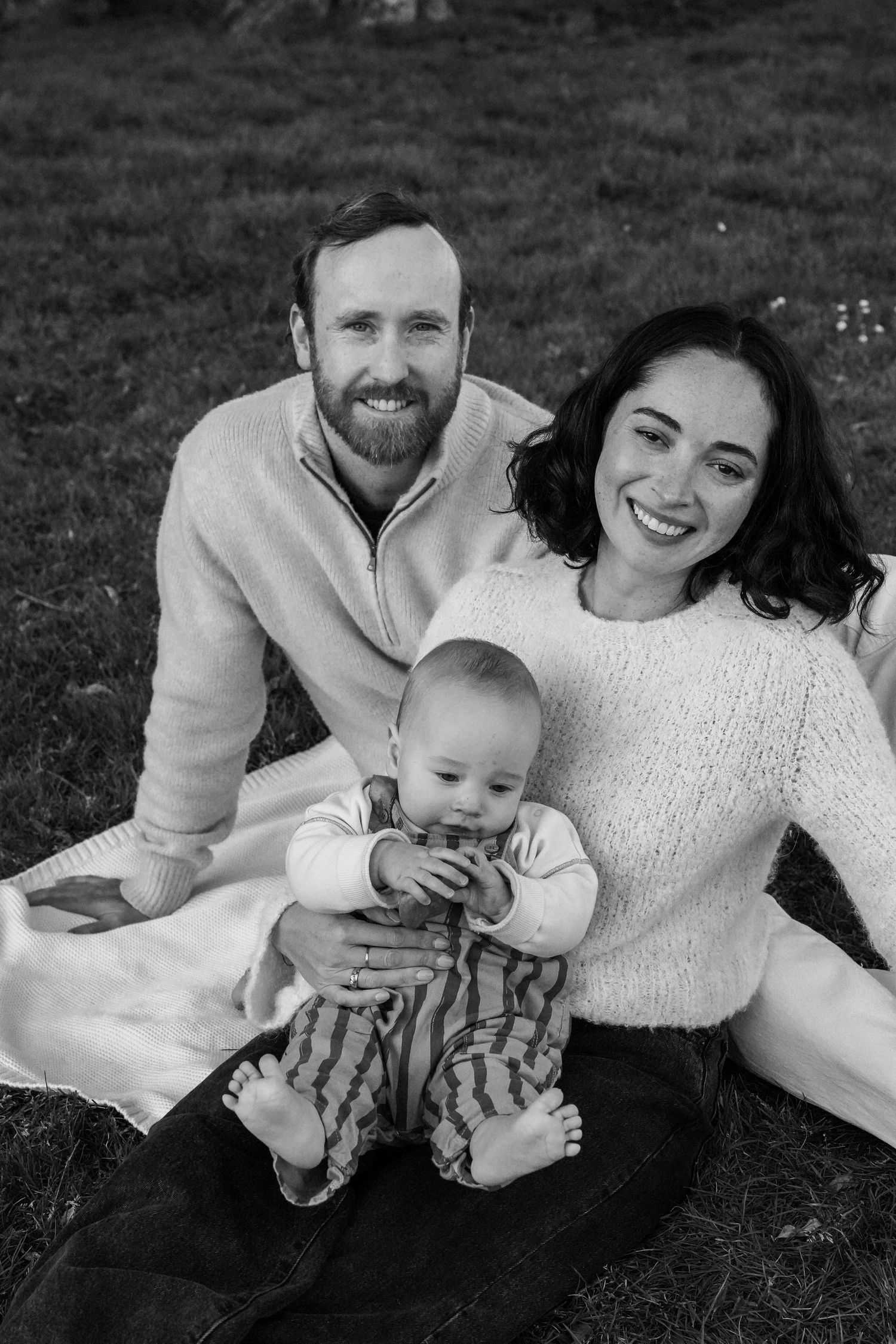 A black and white family portrait taken outdoors on a blanket.