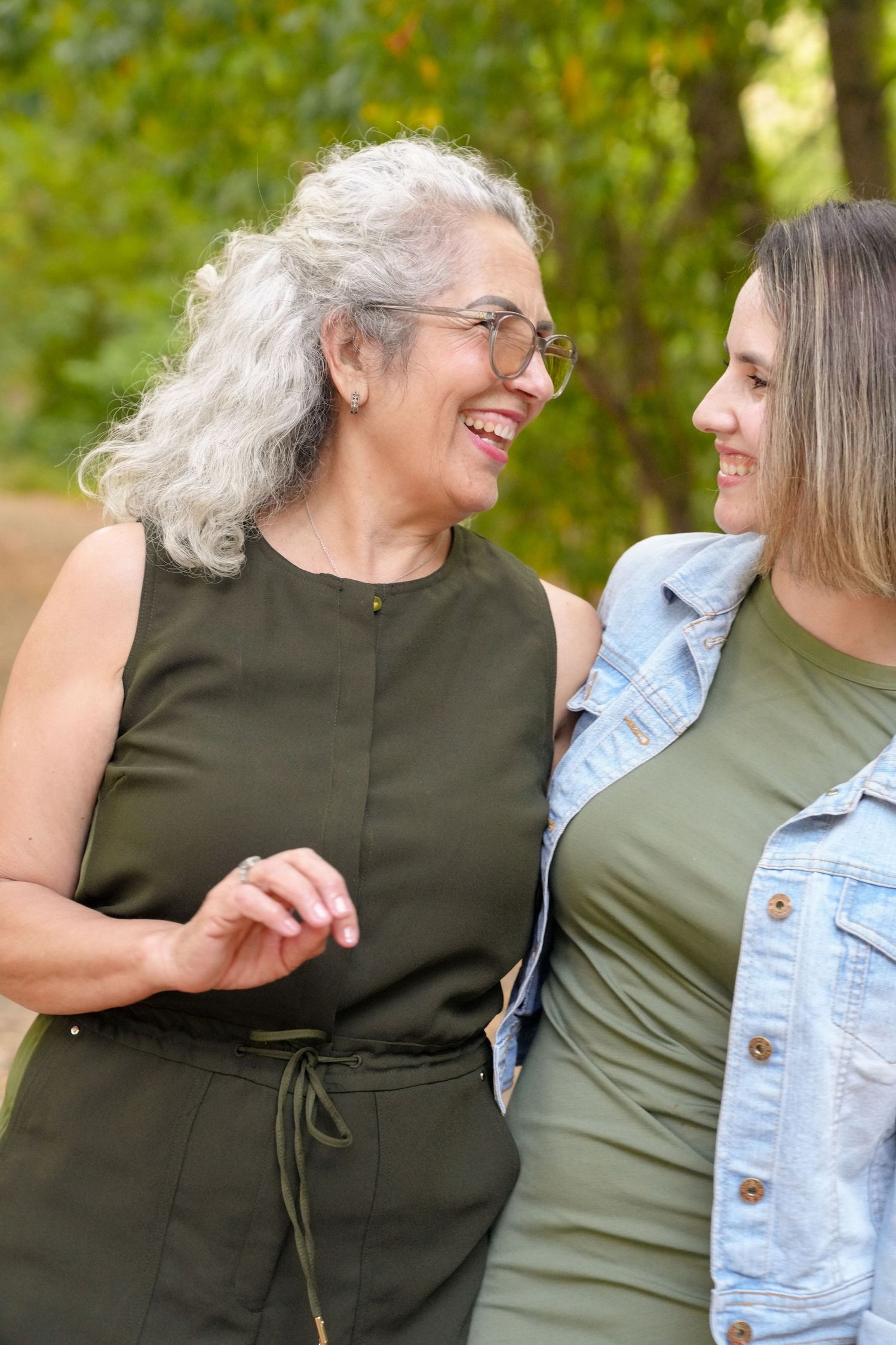 Two people share laughter and smiles while embracing in front of autumn trees.