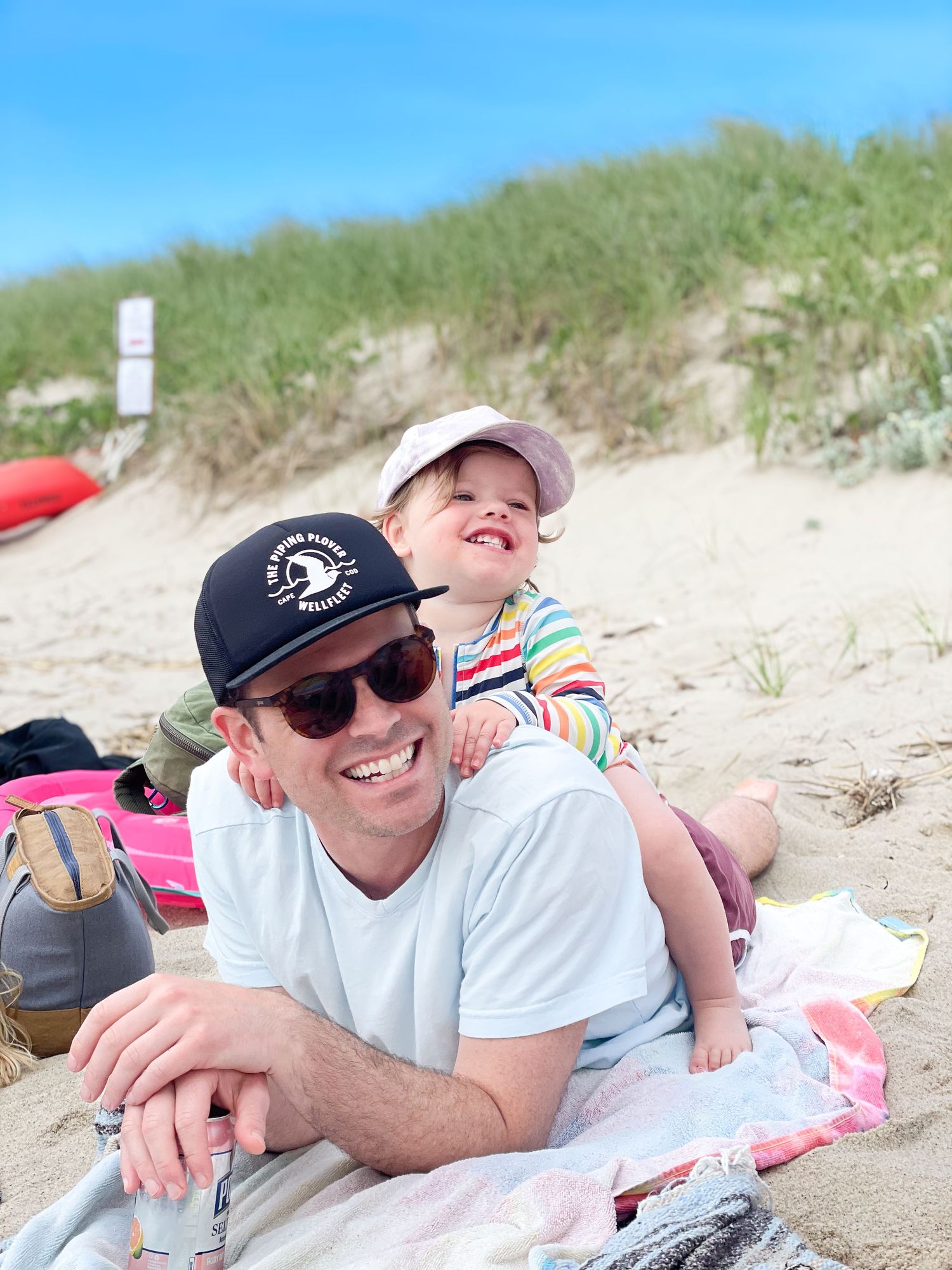 People relaxing at a beach lying on blankets on a sunny day. Sand dunes in background.