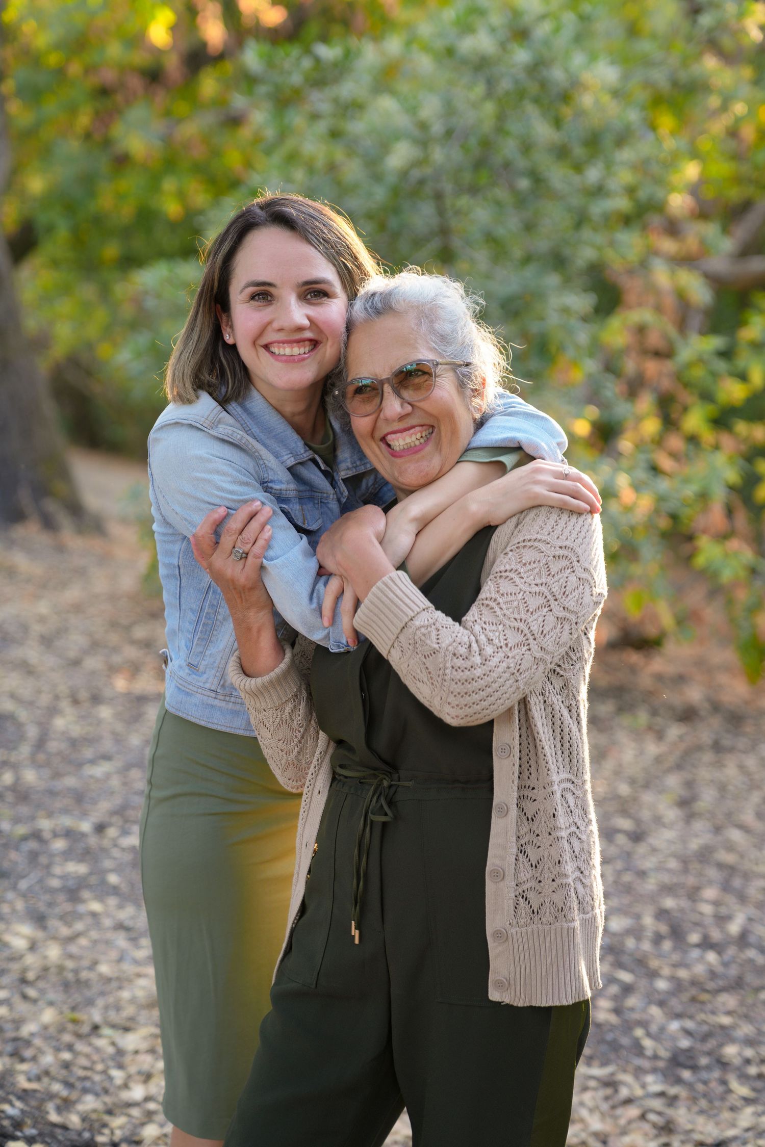Two people share a heartwarming embrace outdoors with autumn foliage in the background.