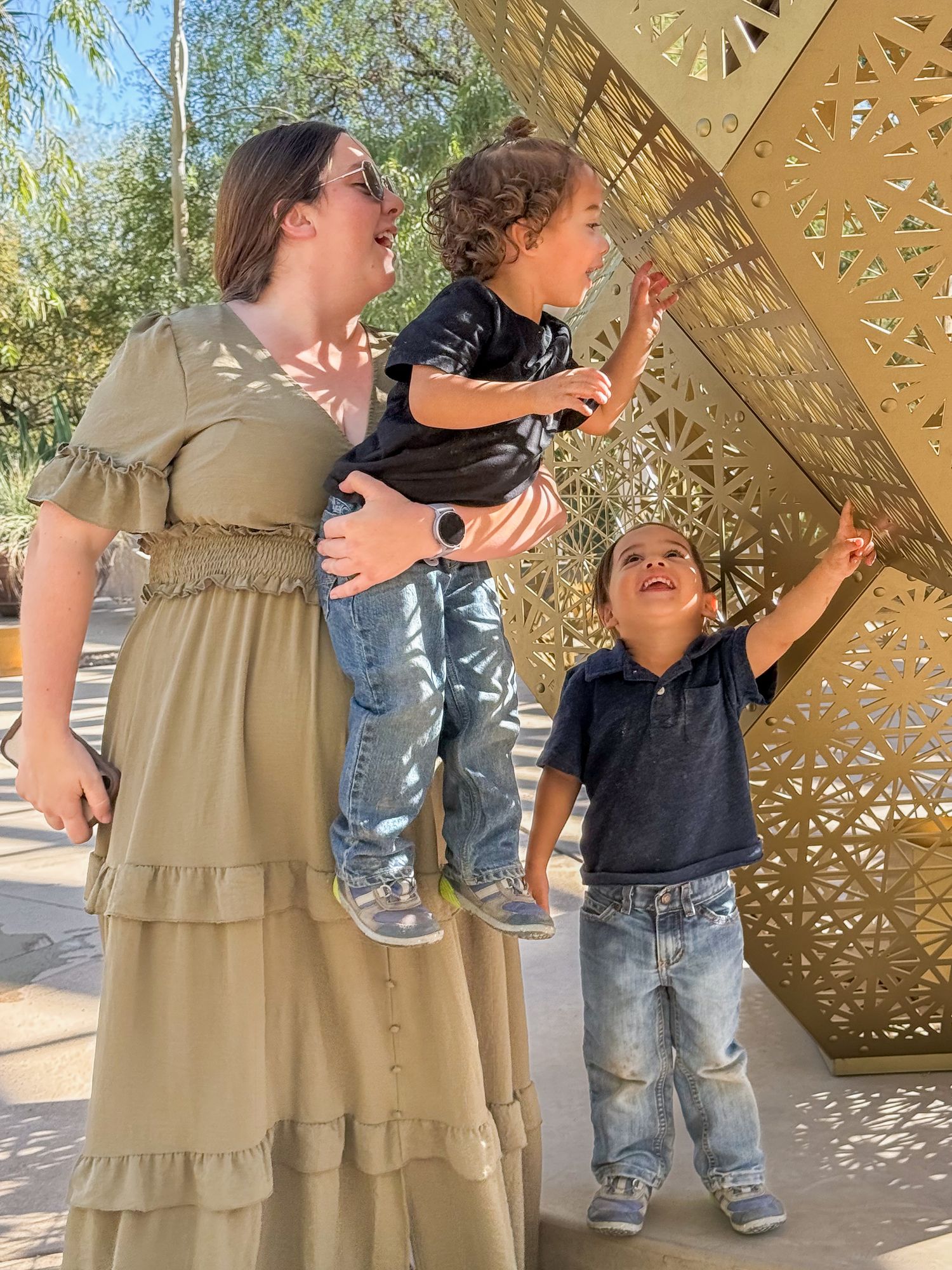 People interacting outdoors under decorative gold lattice sculpture in natural lighting.