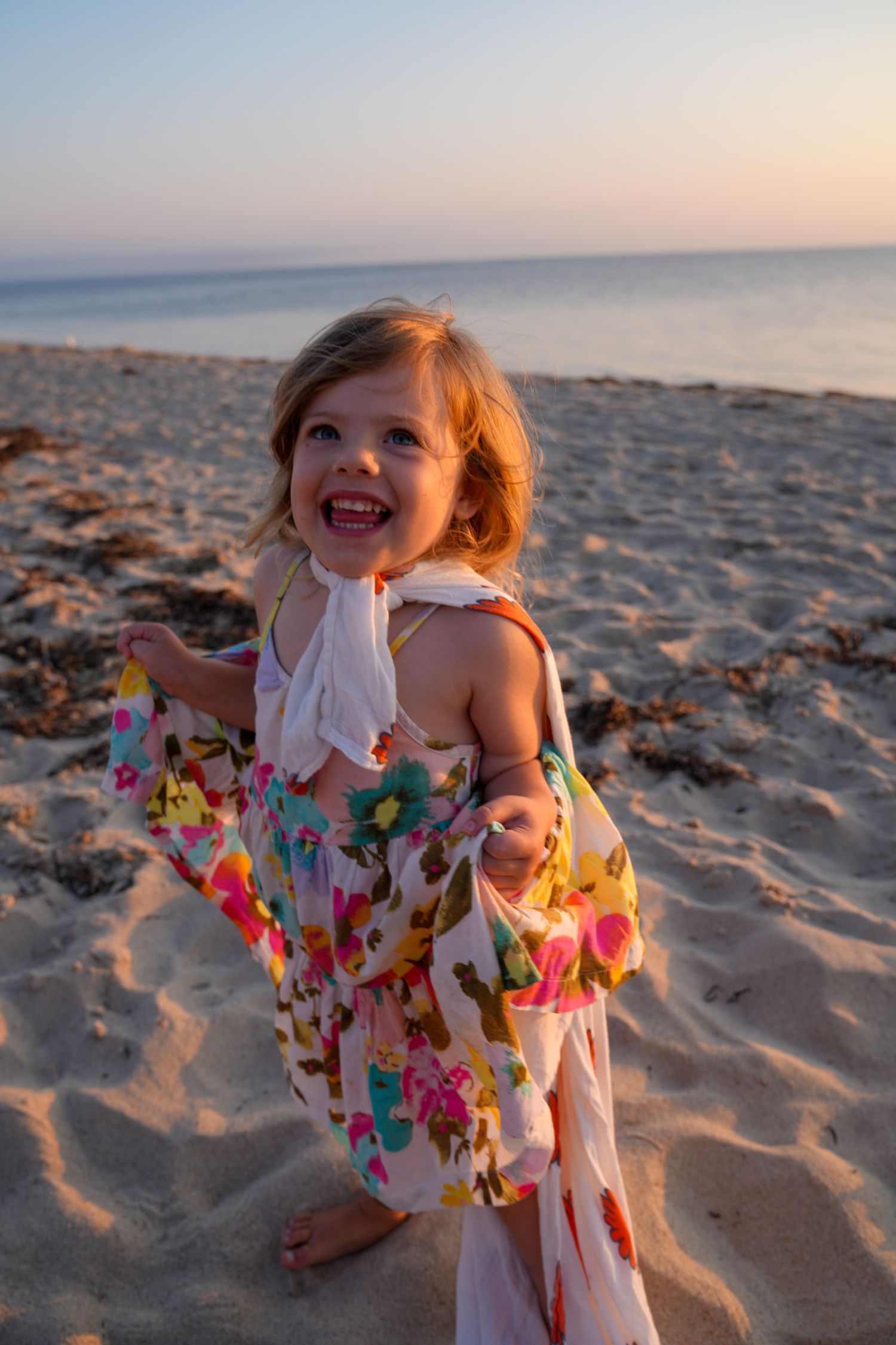 A young child in a colorful butterfly dress plays joyfully on the beach at sunset.
