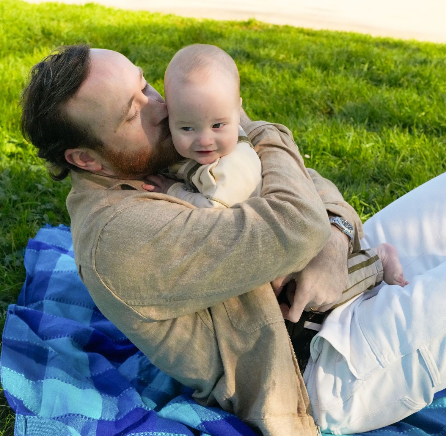 A tender moment shared on a blue blanket in the grass on a sunny day.
