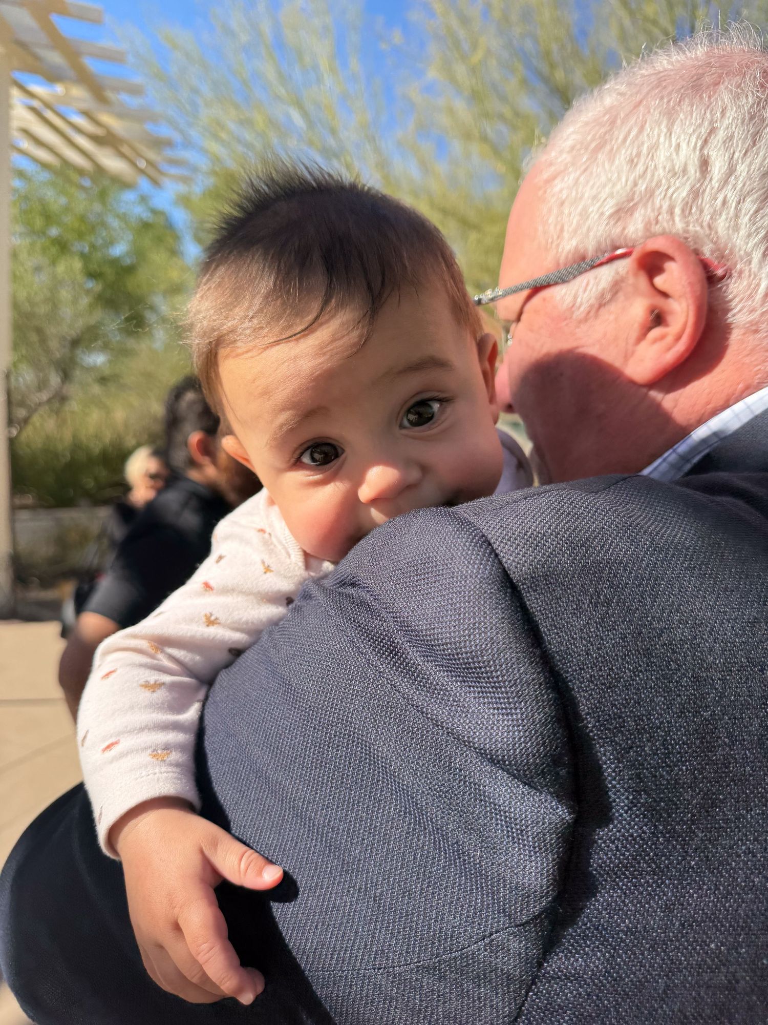 Baby resting against shoulder in grey clothing outdoors.