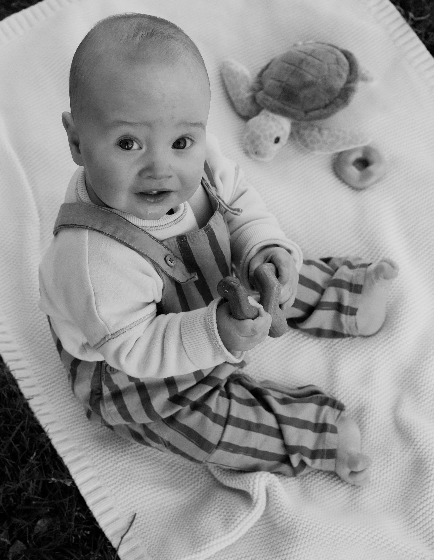 Black and white photo of baby playing with toys on blanket.