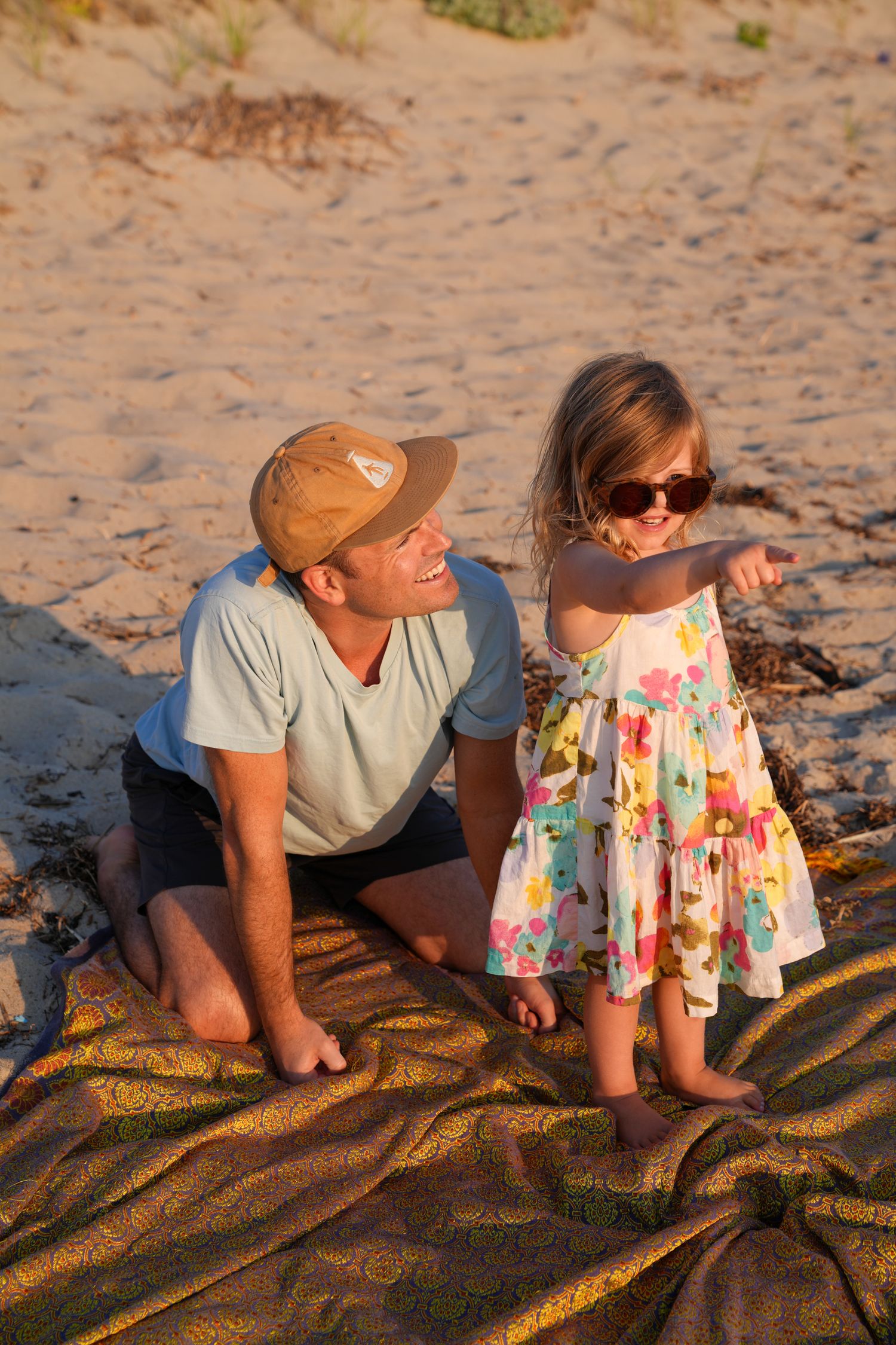 Two people laying on a patterned beach blanket during golden hour at the beach.