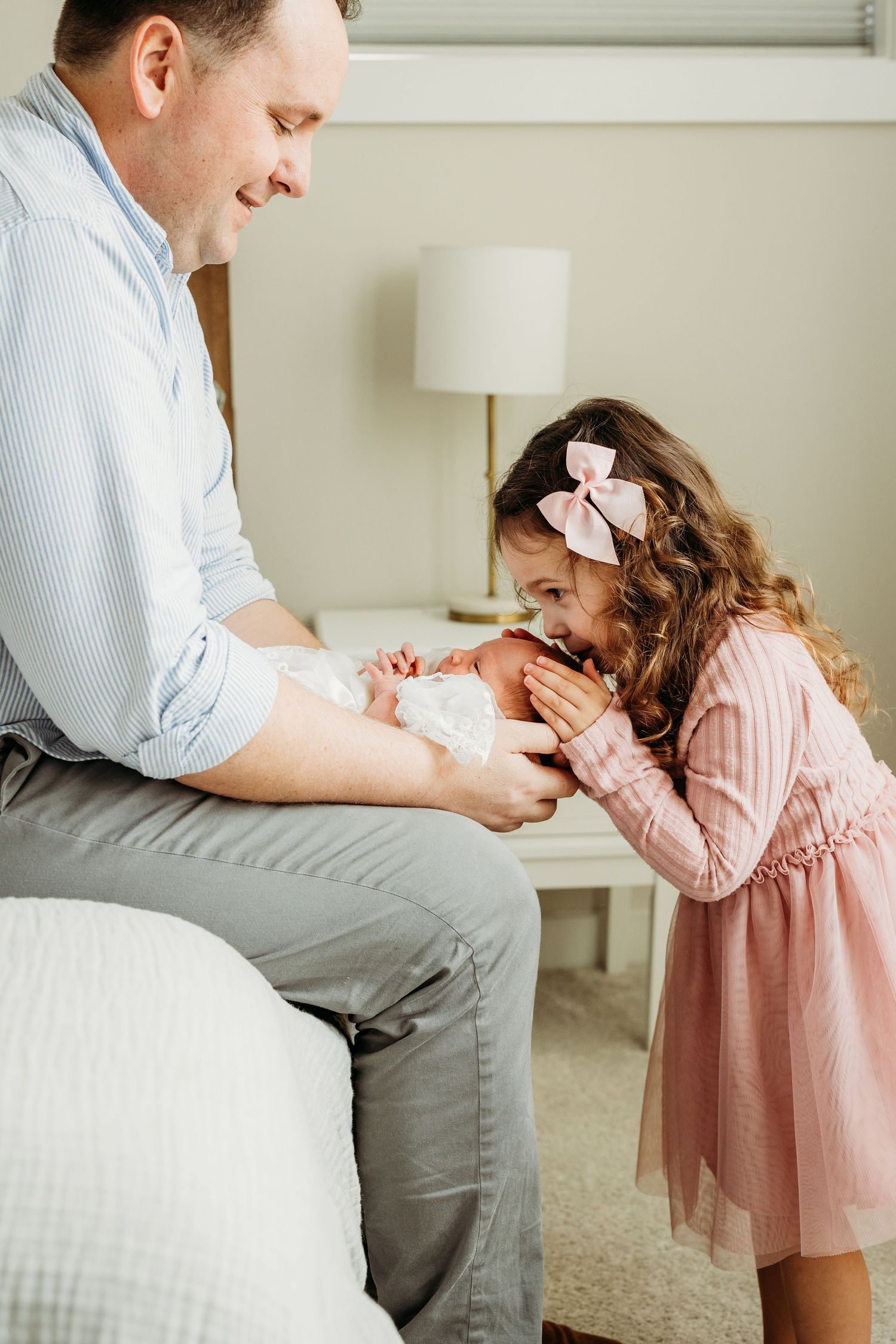 big sister kissing baby sister’s head while dad holds baby