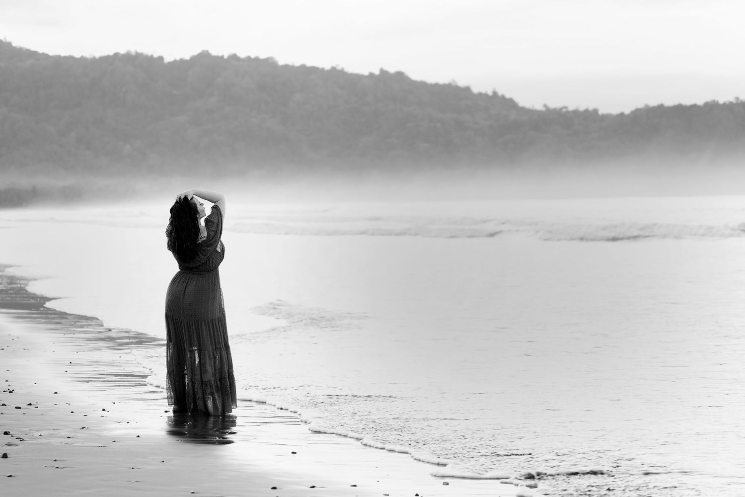 Black and white image of woman standing on a misty beach at sunrise
