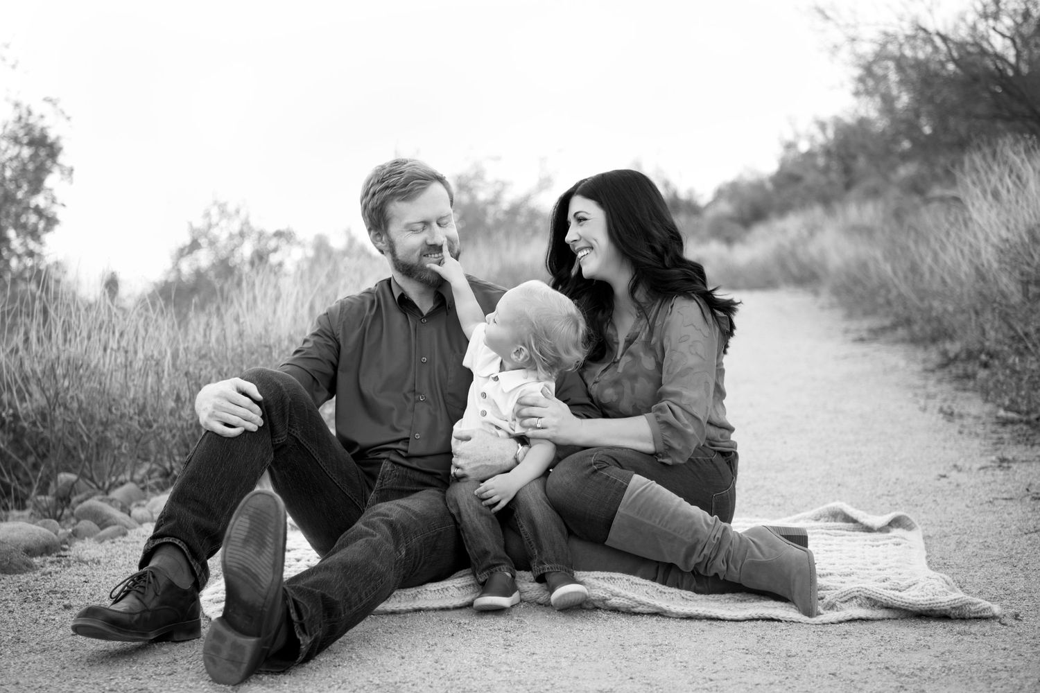 Small young family sits in arizona desert on picnic blanket snuggling young toddler candid image Mesa AZ Usery Mountains Sunset