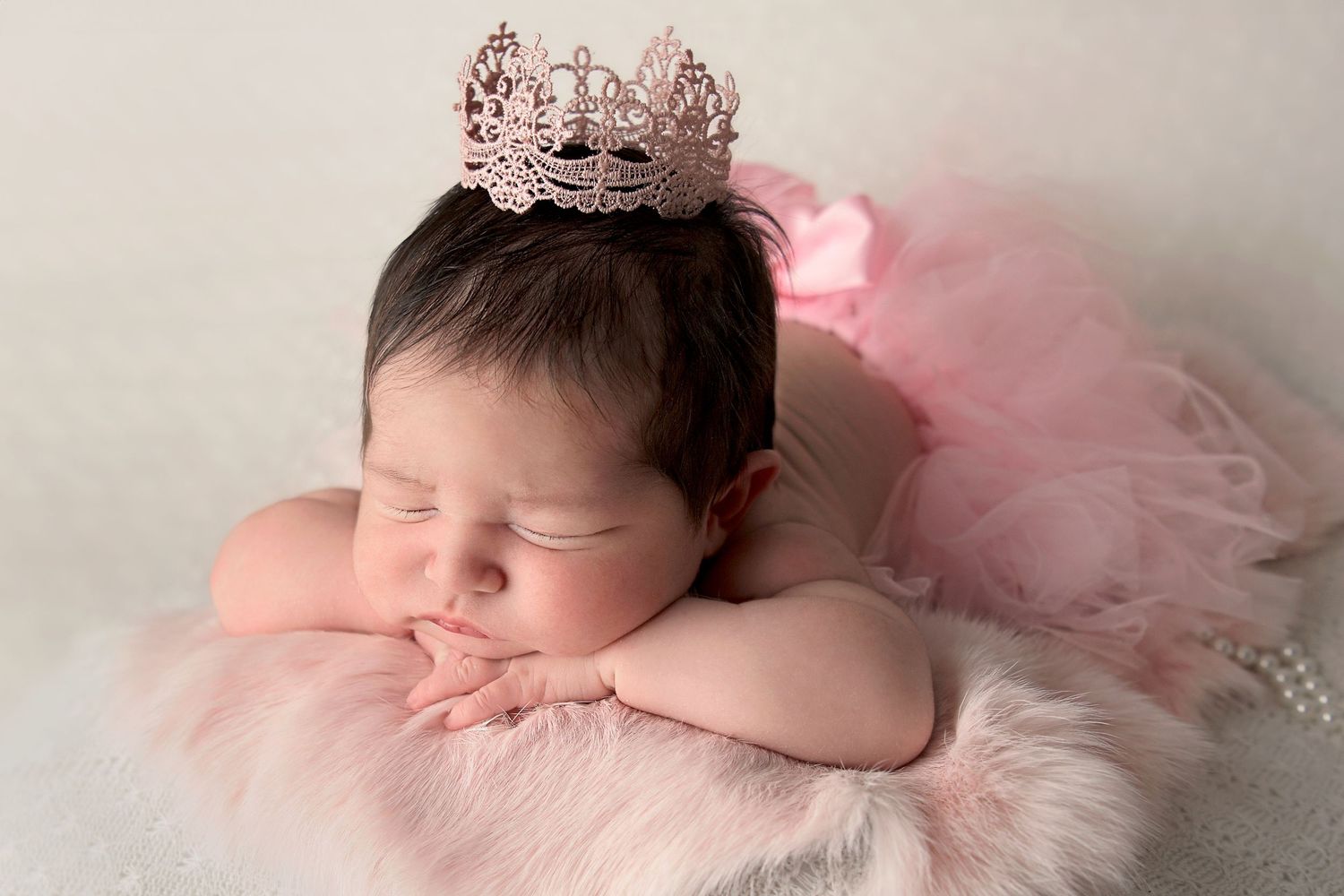 Baby girl surrounded by all pink wearing a princess tiara with chin on hands in newborn photo in Gilbert AZ