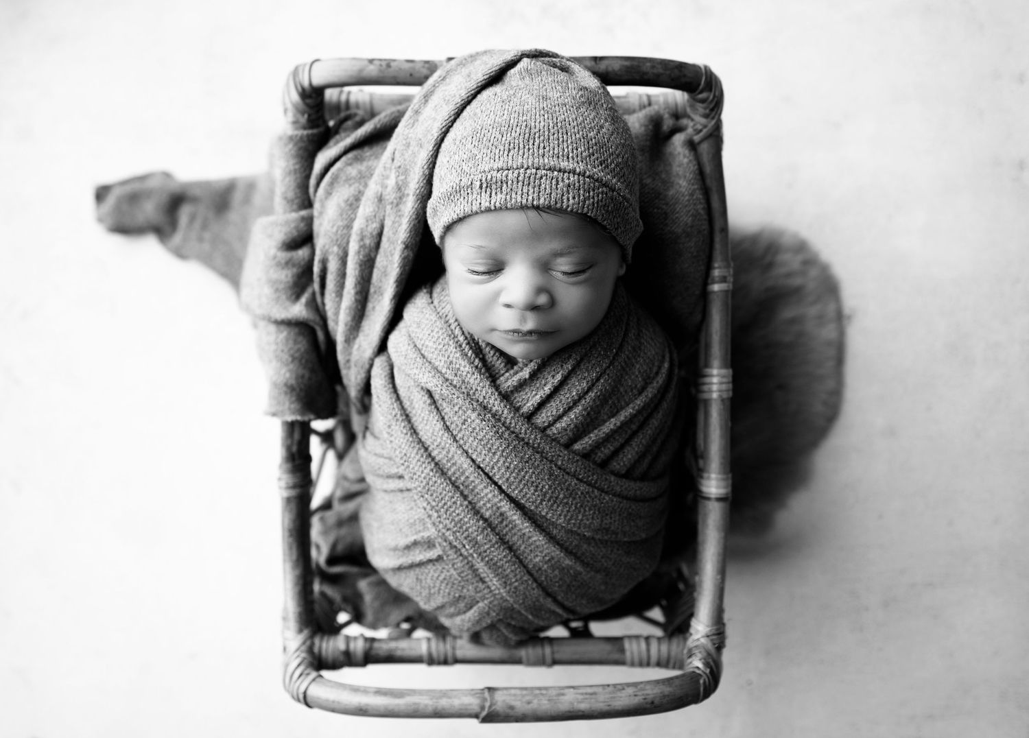 Black and white newborn photo of baby swaddled in grey blanket and sleepy cap in a small prop crib in Scottsdale Arizona