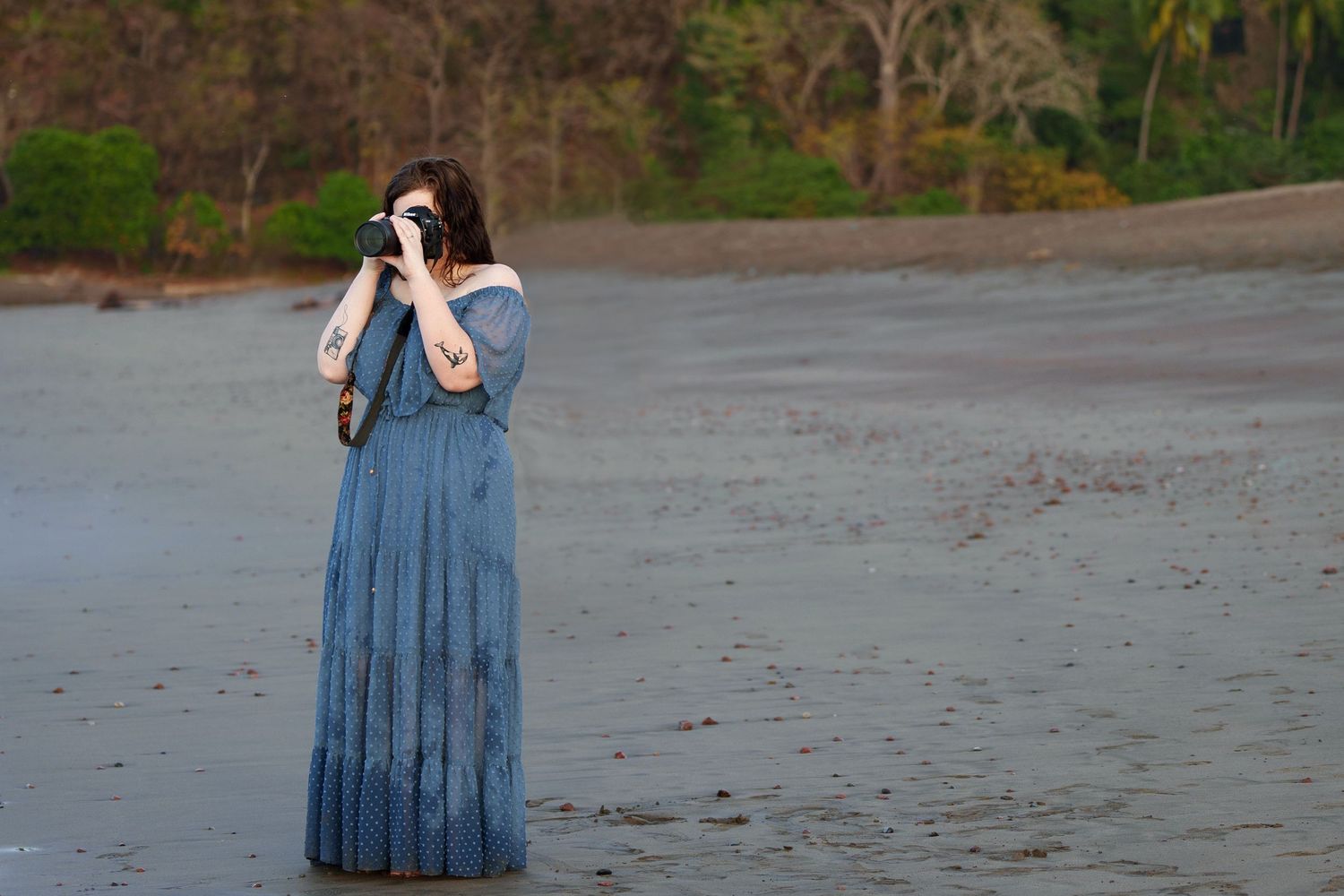 Olivia from Olivia Grace Photography stands in a blue gown on the beach of Costa Rica taking photos