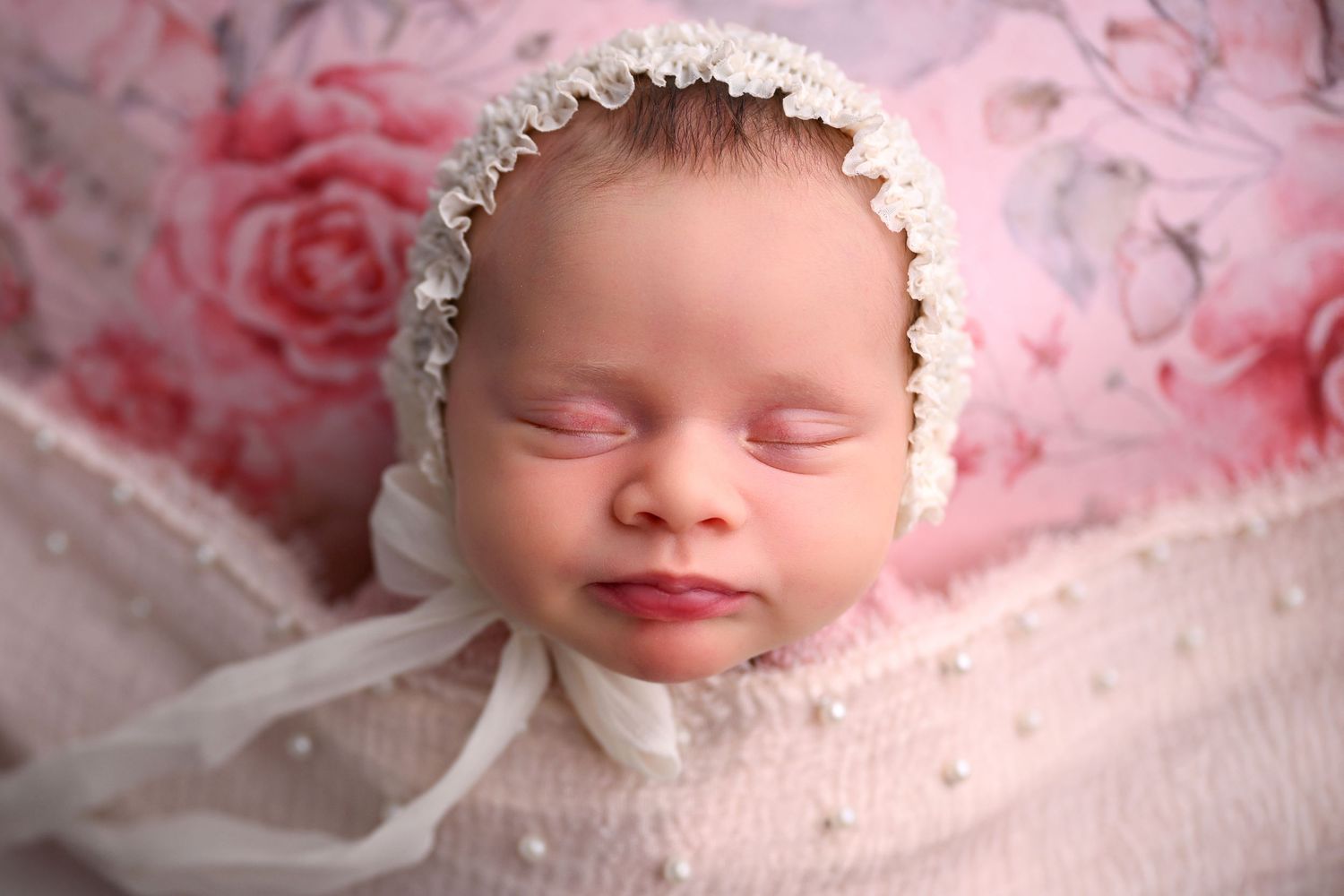 Close up shot of Newborn baby girl with a floral backdrop wearing a cream bonnet with bow