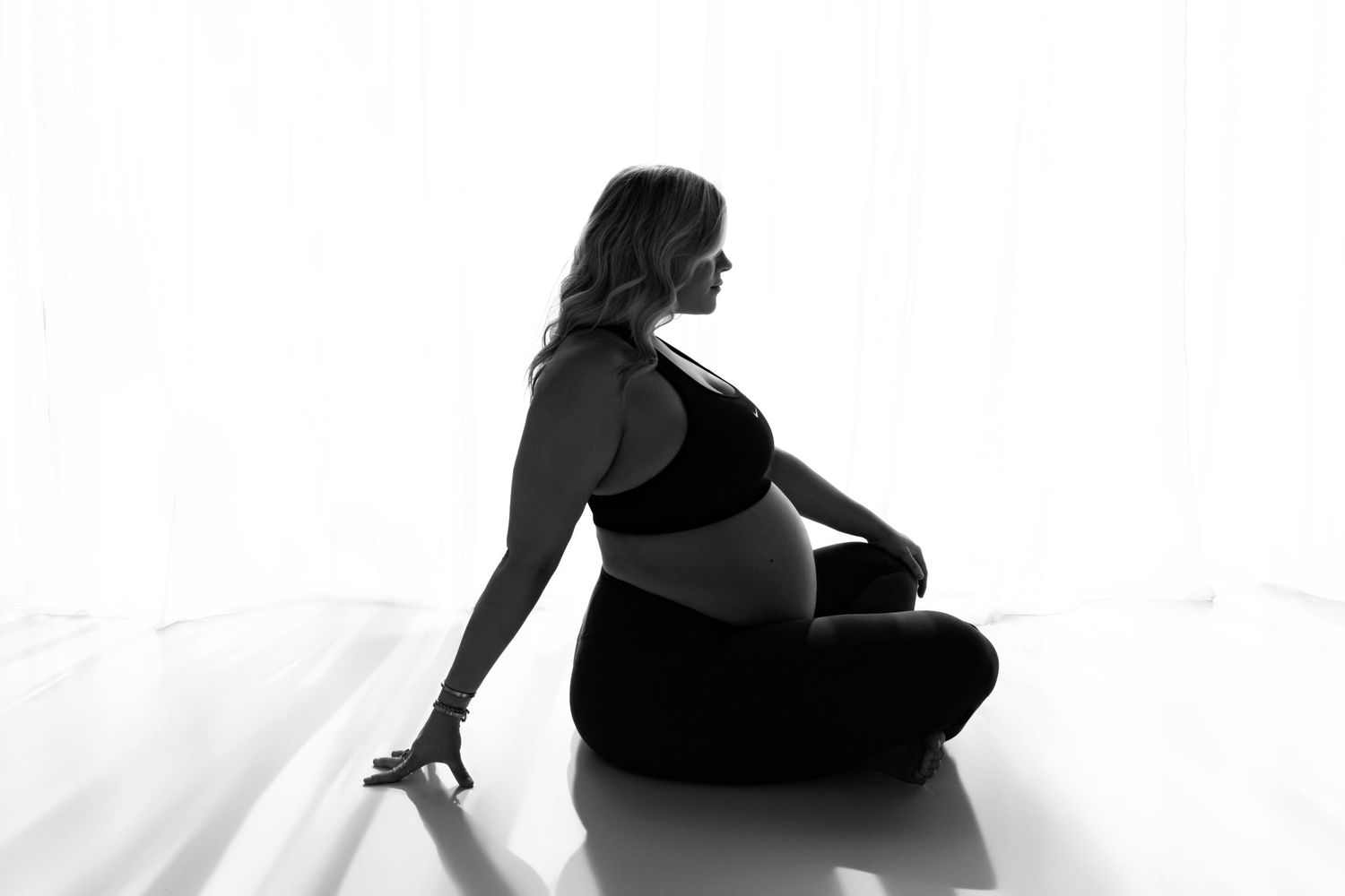 Pregnant woman doing yoga and meditating with hands on belly in a tranquil backlit studio in phoenix
