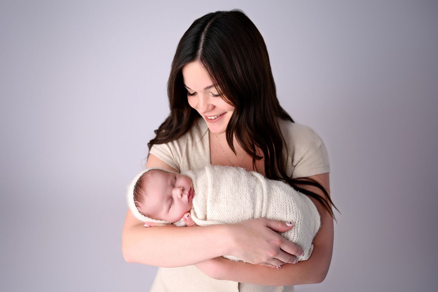 Mother smiles down at brand new baby boy who is swaddled up in knit neutral banket