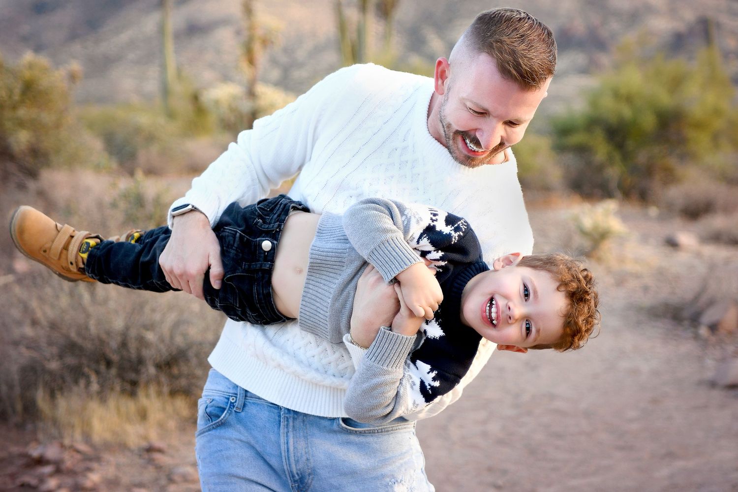 Parents lifting their toddler in the air during a sunny outdoor session.