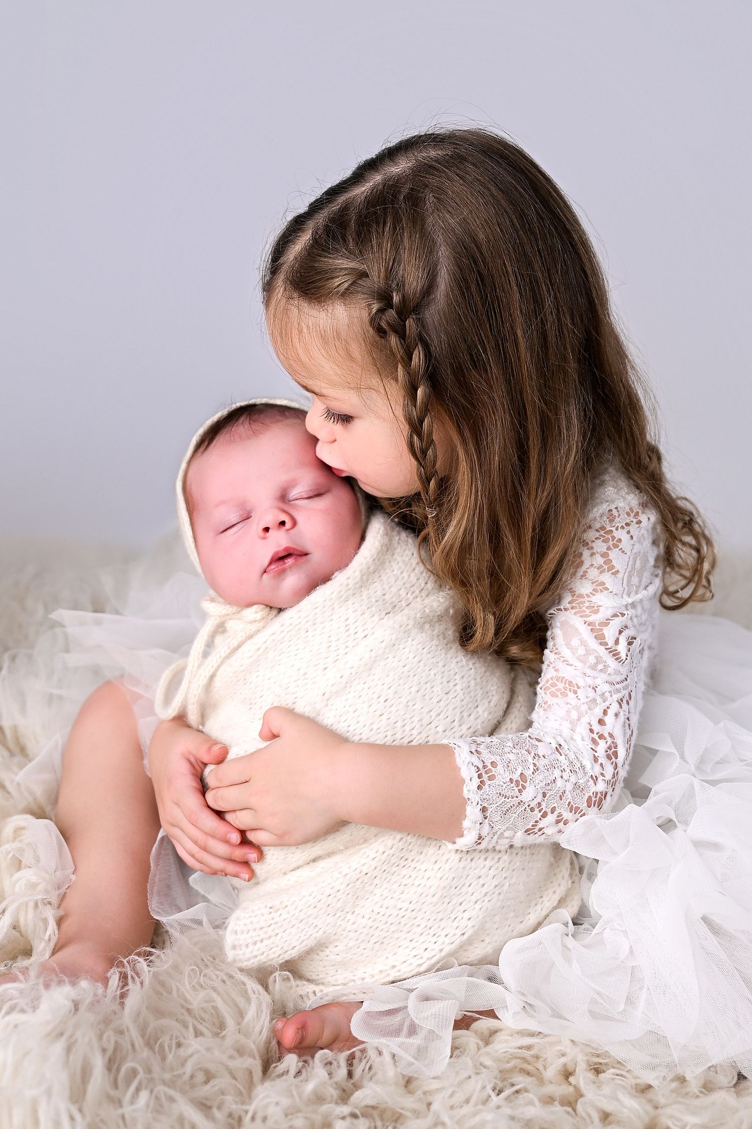 Big sister holds and kisses baby brother's temple