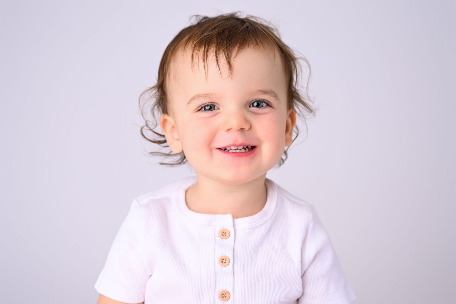 Image of smiling toddler on white backdrop in Phoenix Photography studio by Olivia Grace Selin of Olivia Grace Photography