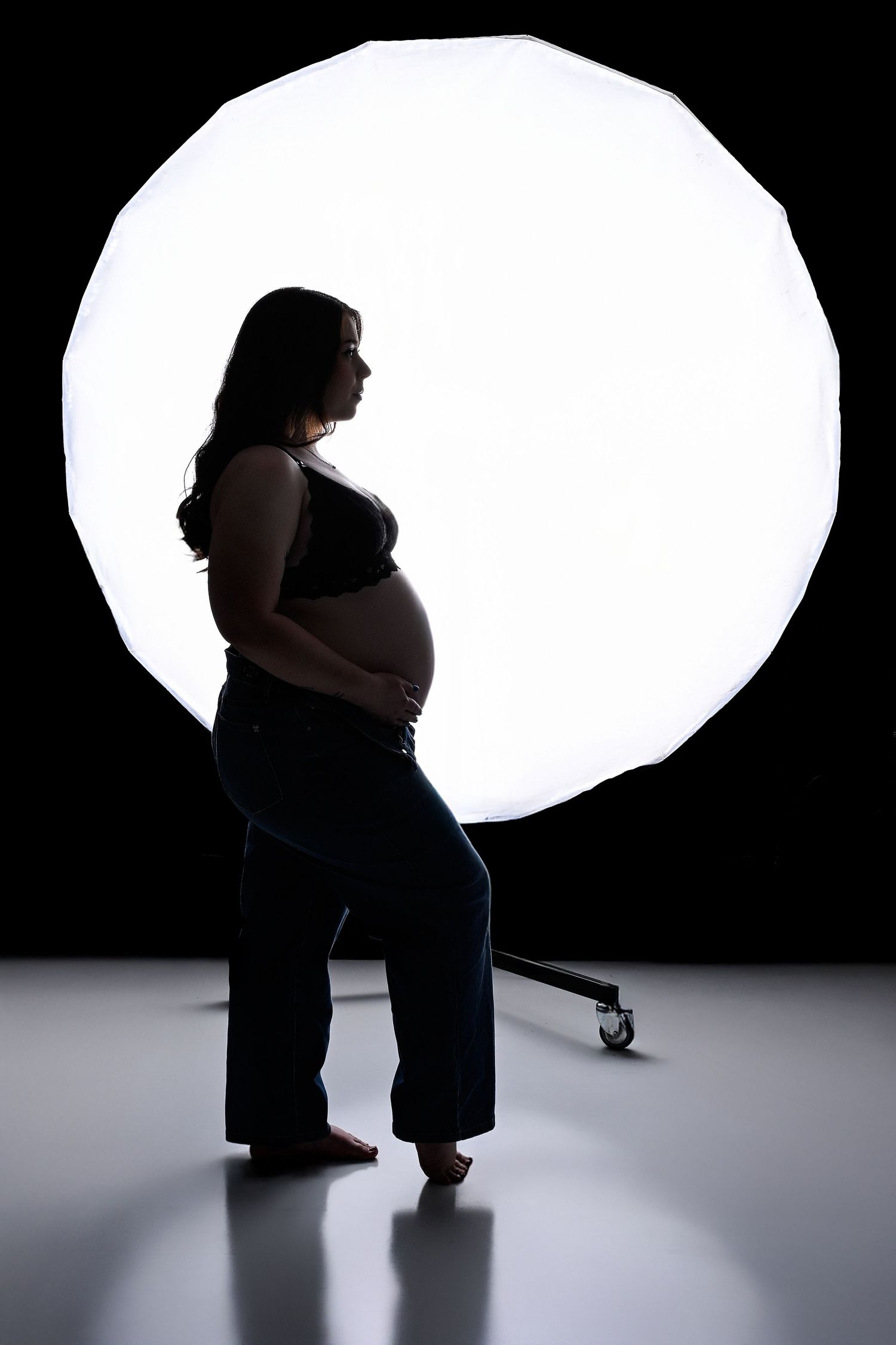 An industrial/artsy silhouette Maternity photo. The side profile of the mother is showing with a large round flash behind her