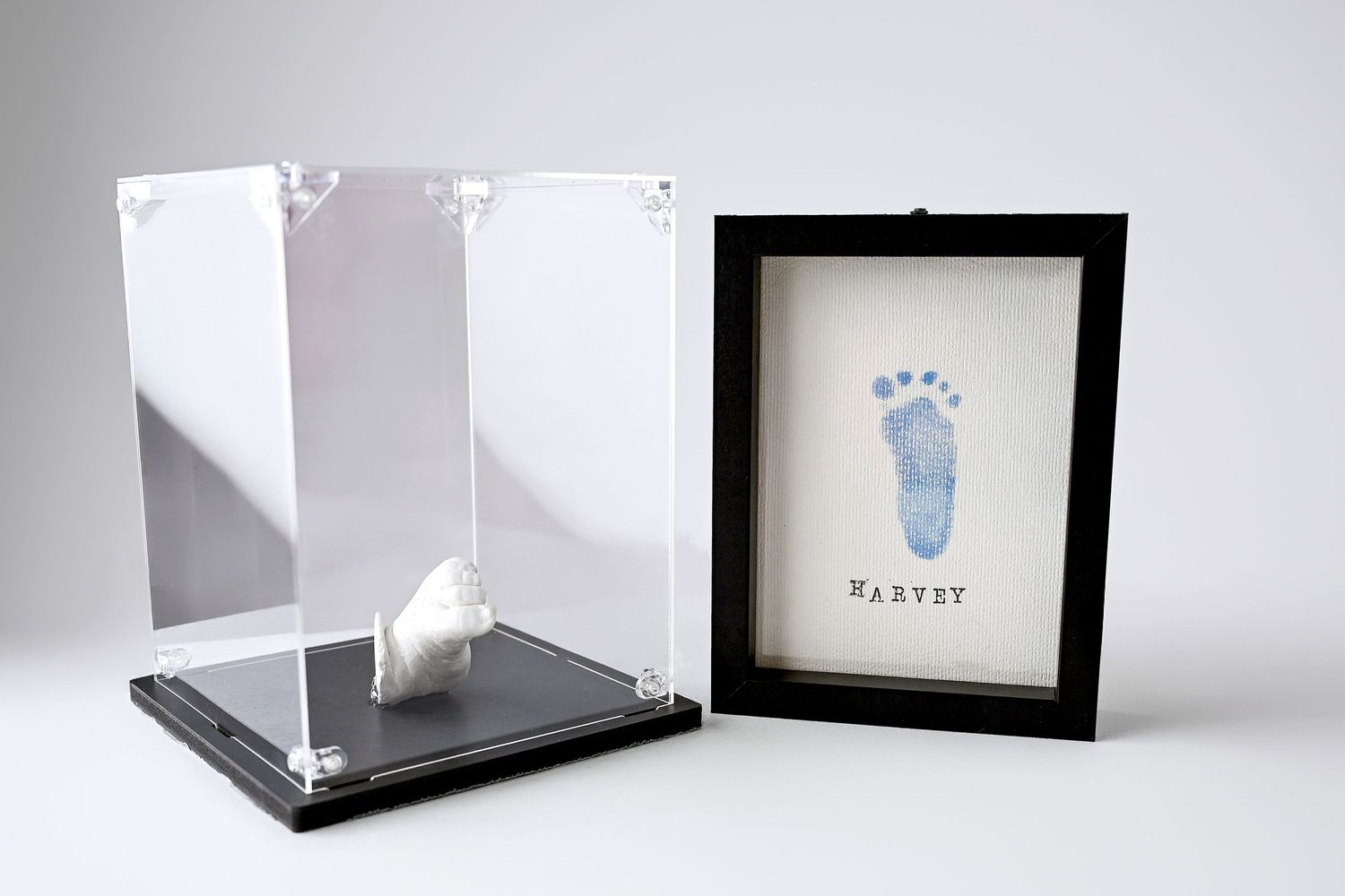 A collection of handmade keepsakes of a newborn baby. A framed footprint with the name Harvey on it and an acrylic art box with casting