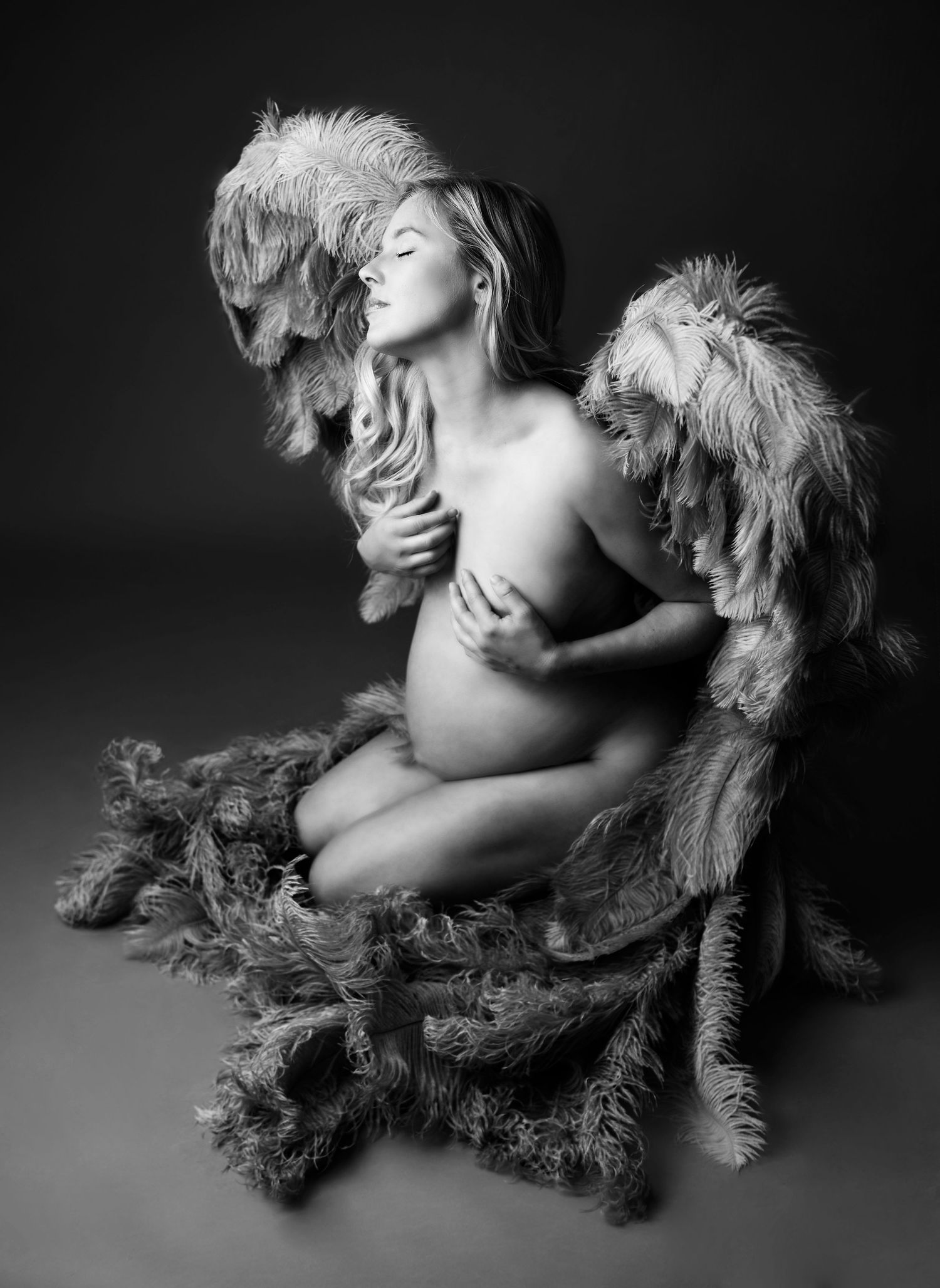 Artistic boudoir image showing a woman wearing angel wings nude in studio.