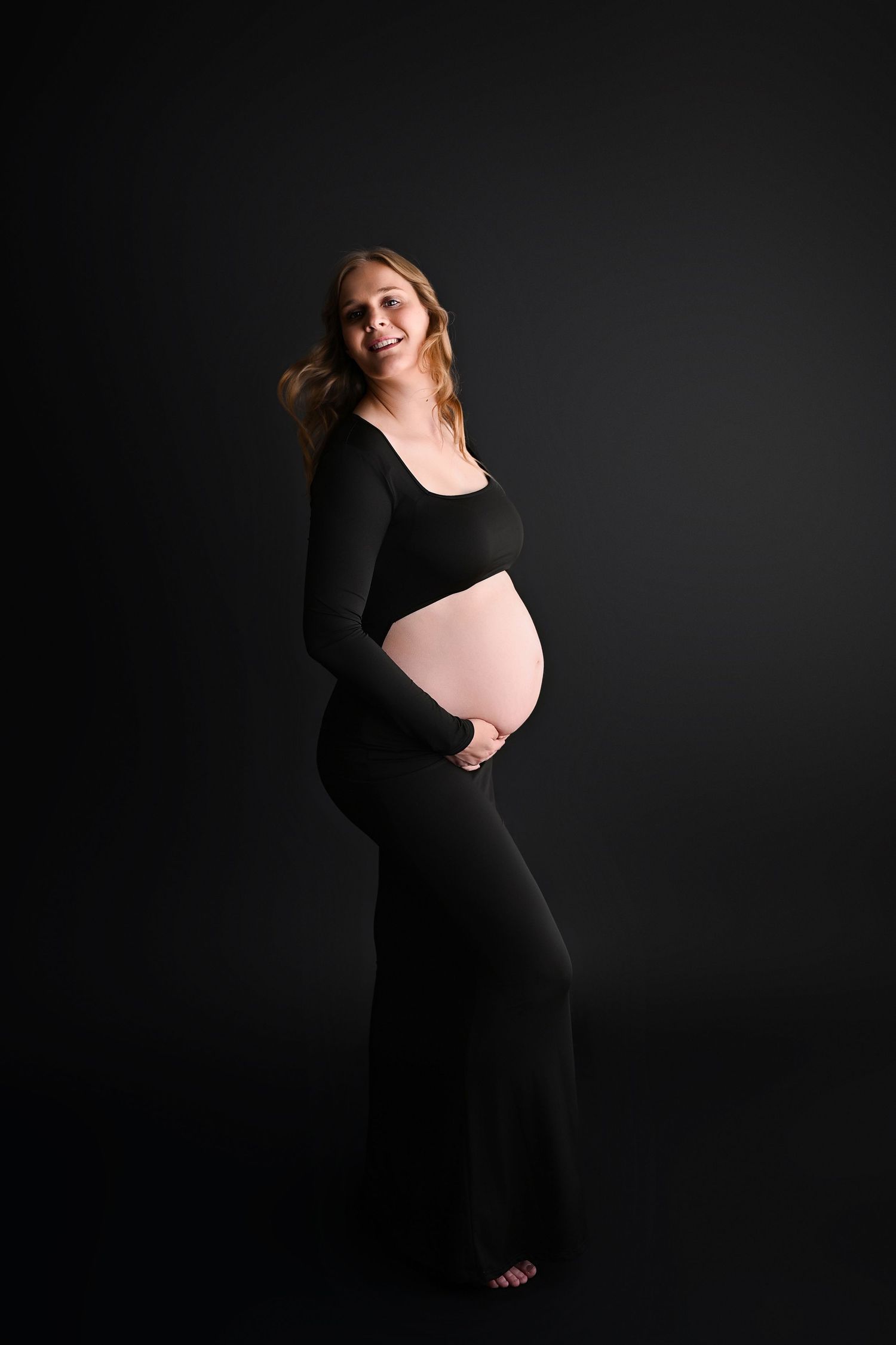 Studio maternity portrait of a woman with a soft spotlight.