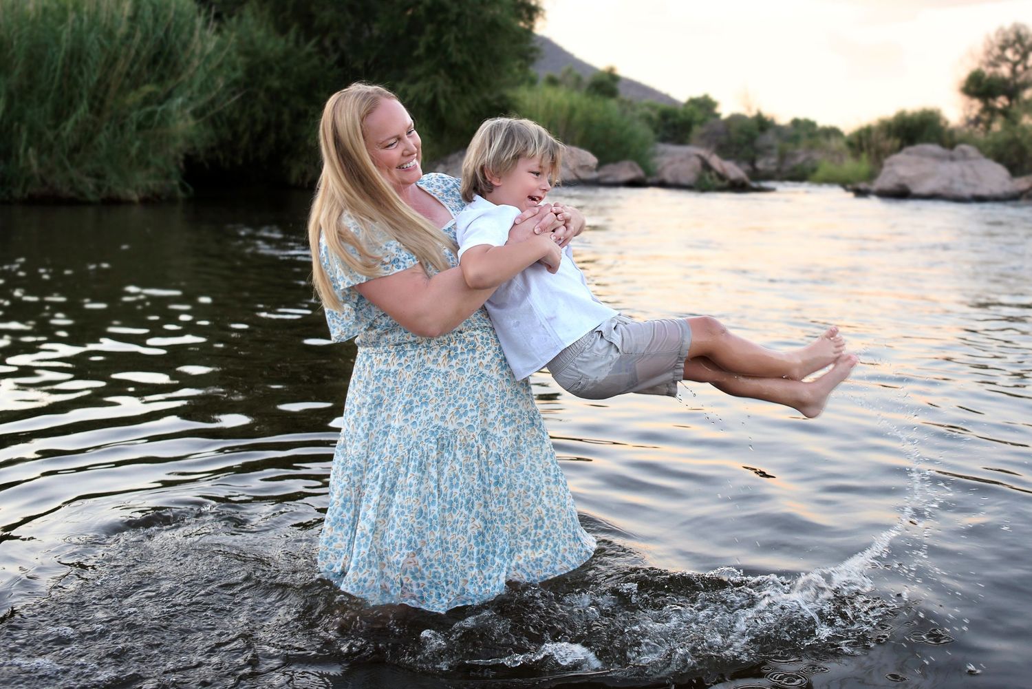 Mother tosses laughing young boy into the river in Mesa Phoenix Arizona Salt River Candid Family photo sunset time over the water