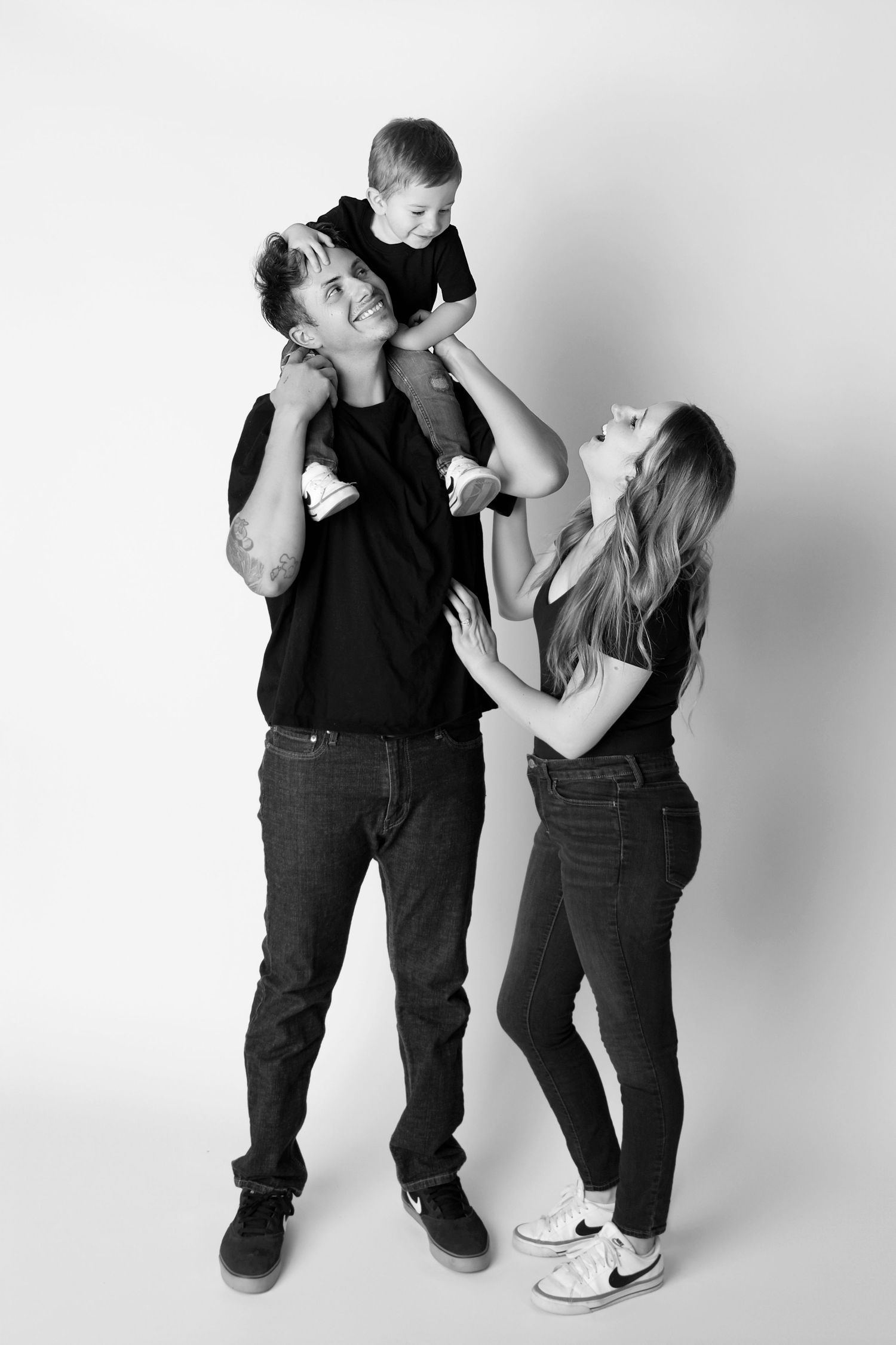 Small family of three laughs at their toddler up on daddys shoulders