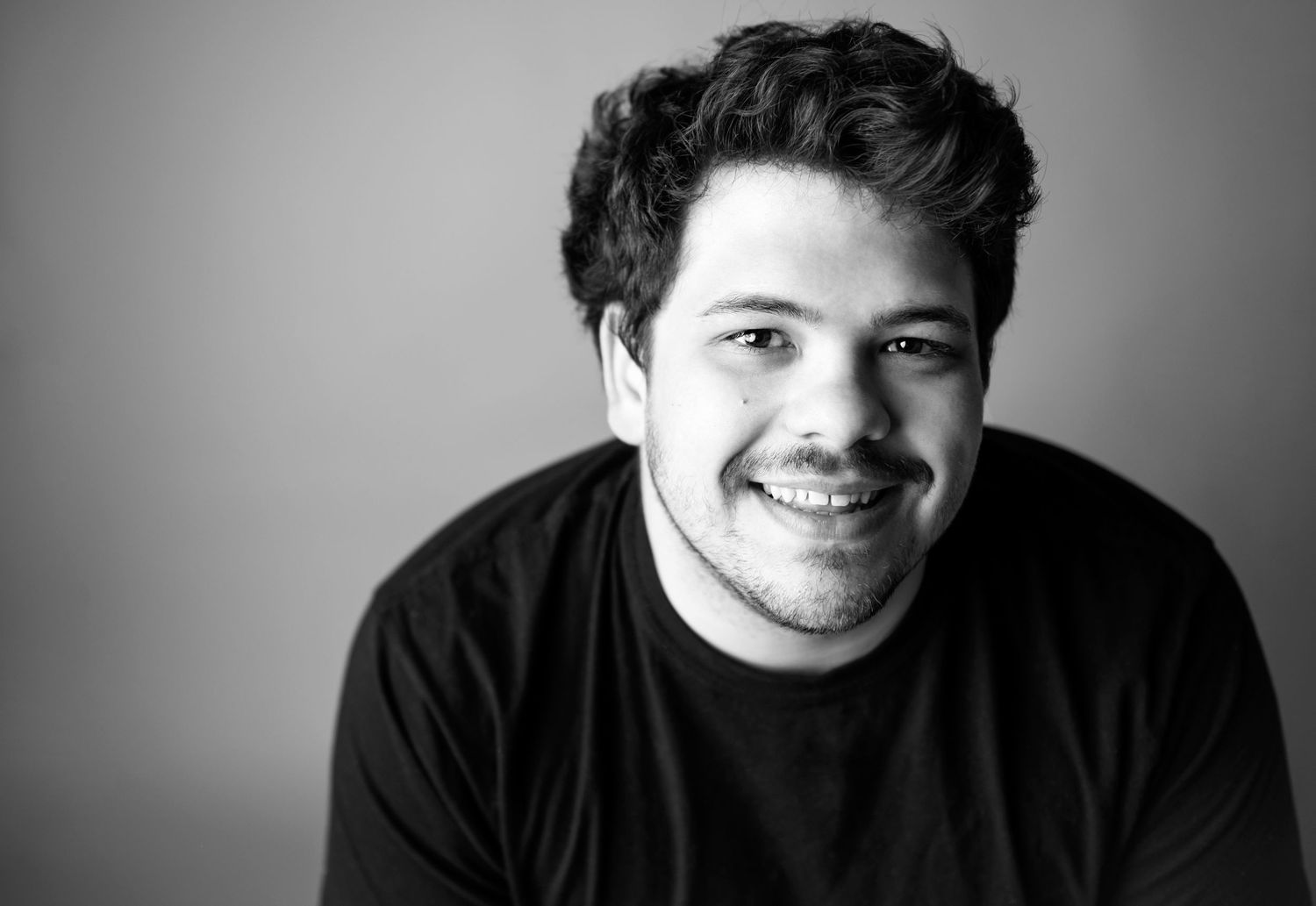 Casual yet polished headshot of a man in a sweater, smiling warmly in natural outdoor light.