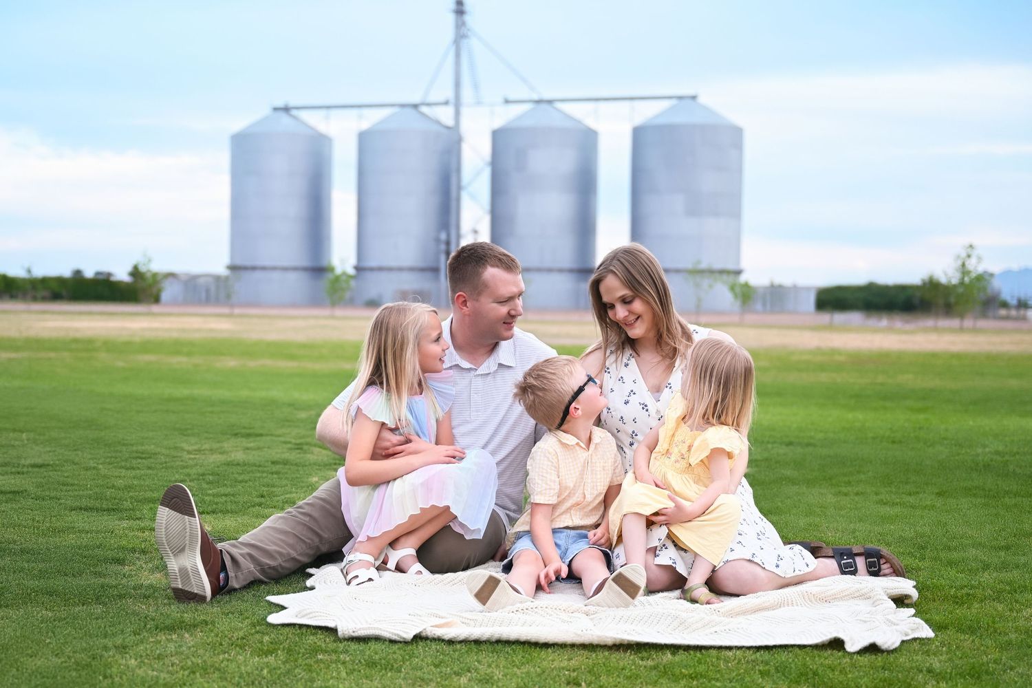 Family sitting on a blanket under a tree during a fall photoshoot with silos in the background