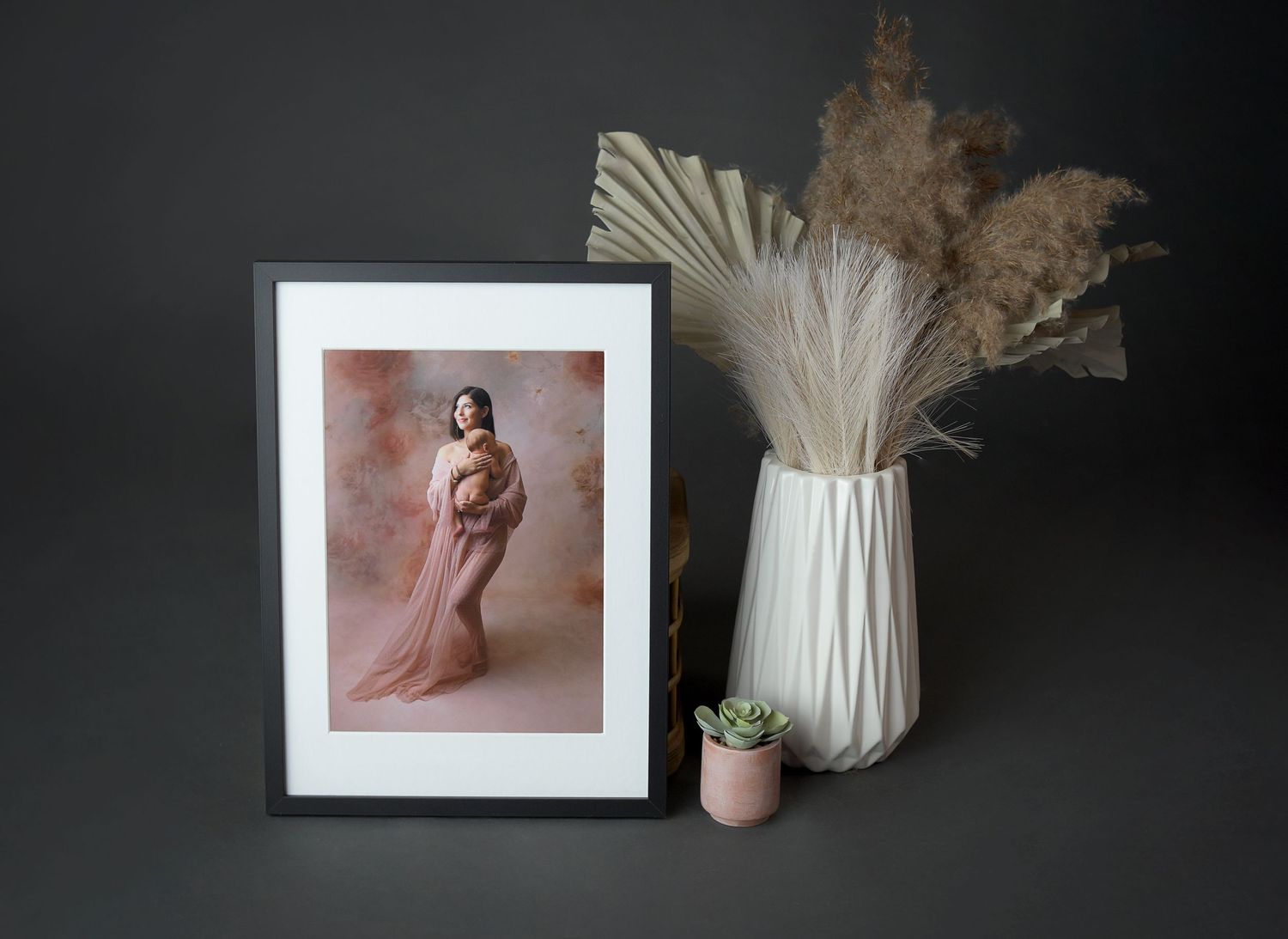 A printed and framed image of a mother holding her newborn. The frame is in a boho flatlay