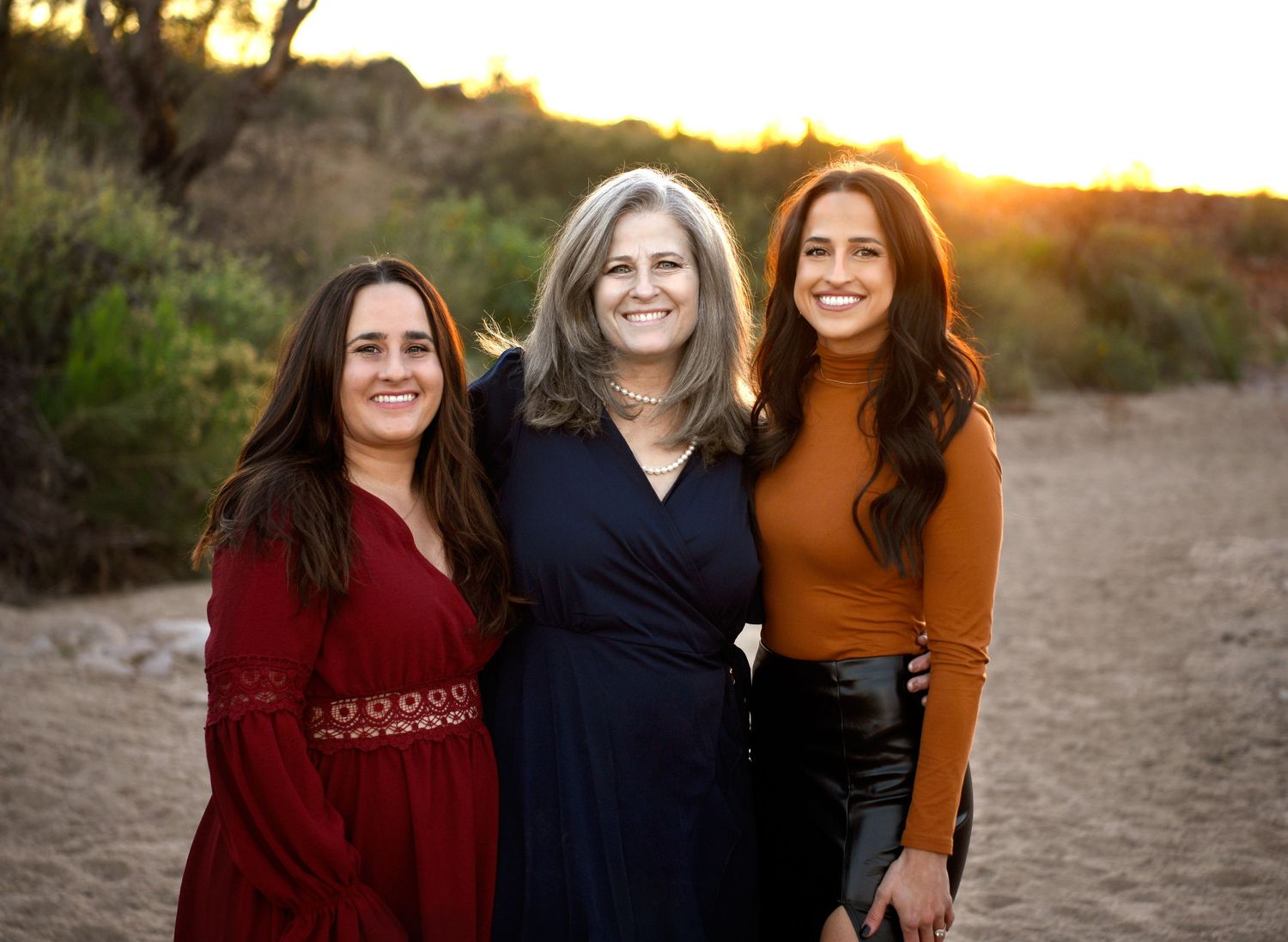 Mother and adult daughters stand posing at sunset smiling in the arizona sun.
