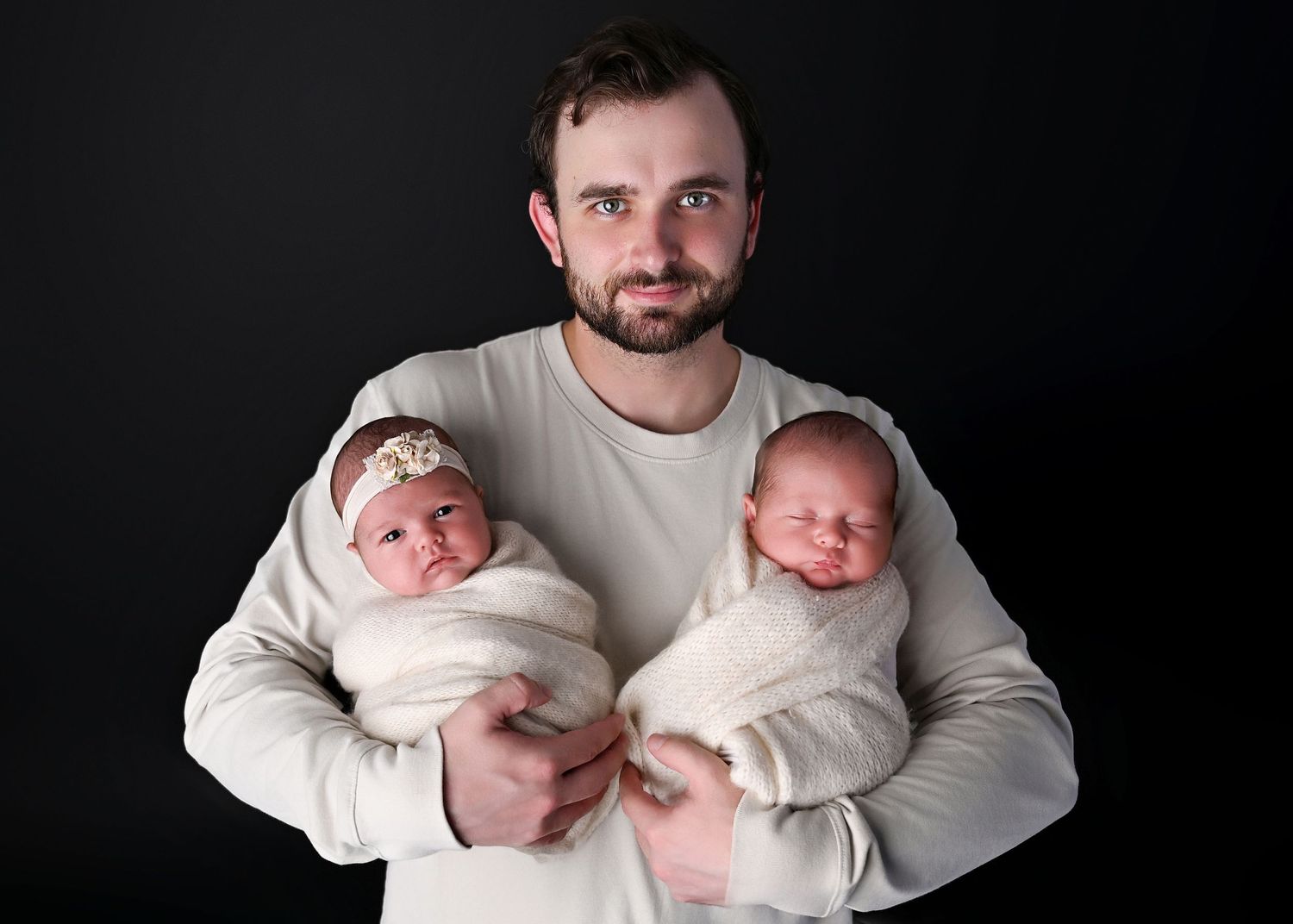 Father holds twin newborns swaddled up