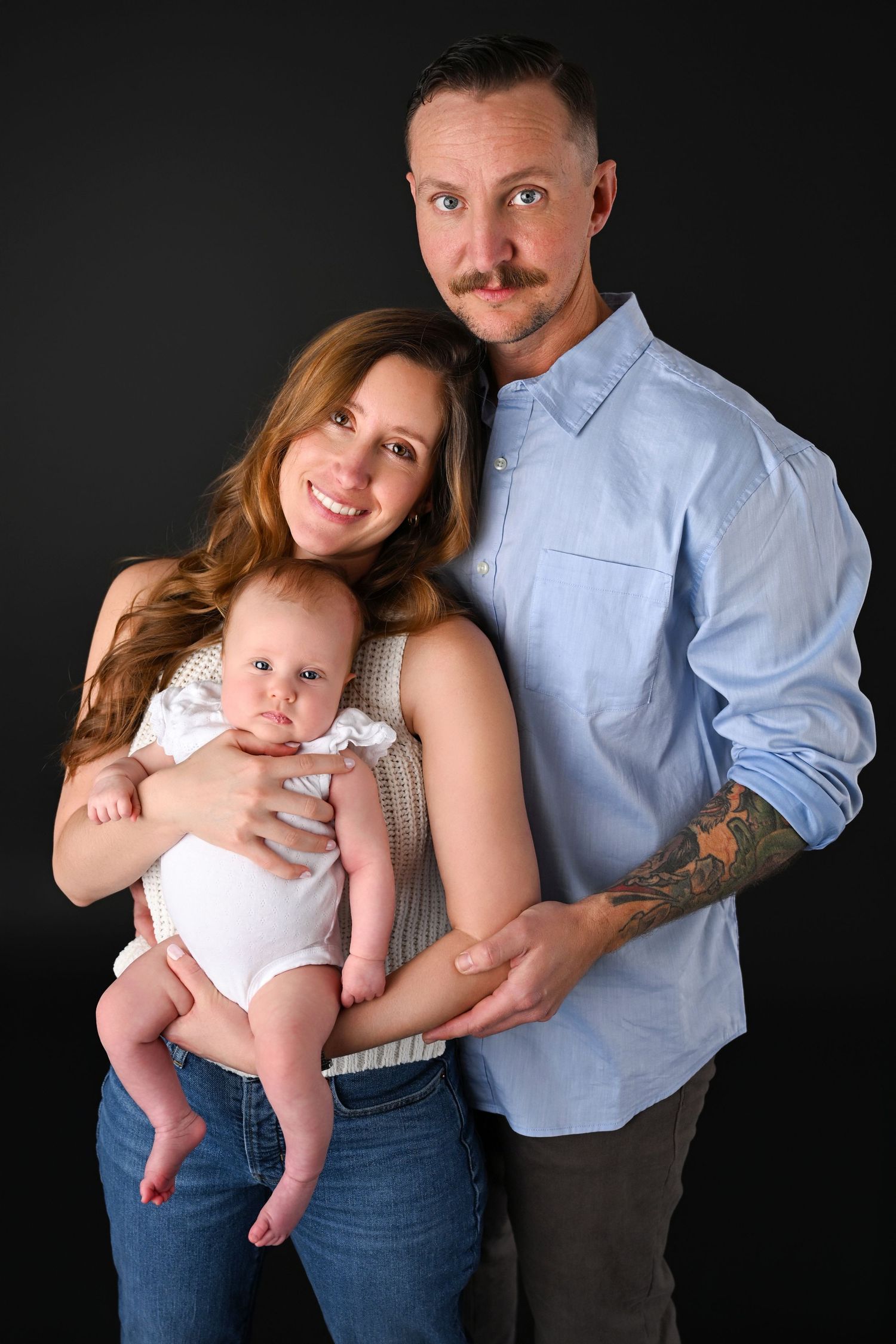 Parents kissing their baby in a cozy studio setup.