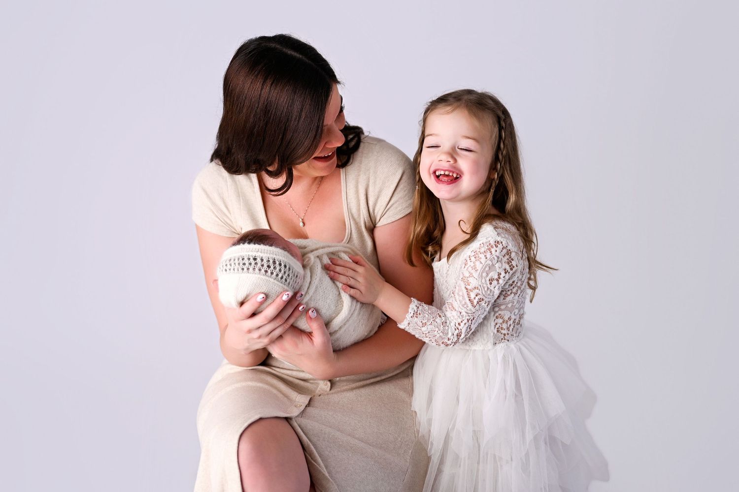 Mother holds newborn baby boy while candidly laughing with toddler daughter