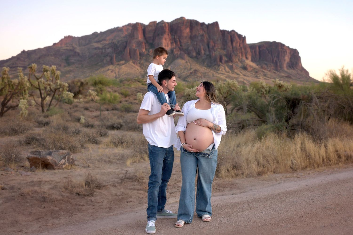 Maternity photo of a young family at the Superstition Mountains in the Arizona Desert. Pregnant Mom with husband and son stand lovingly