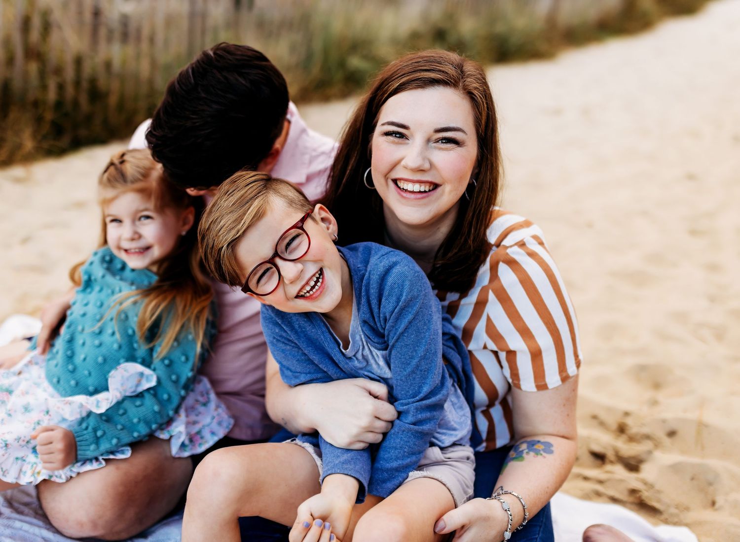 Family of four smiles at the camera sitting outdoors in the sand.