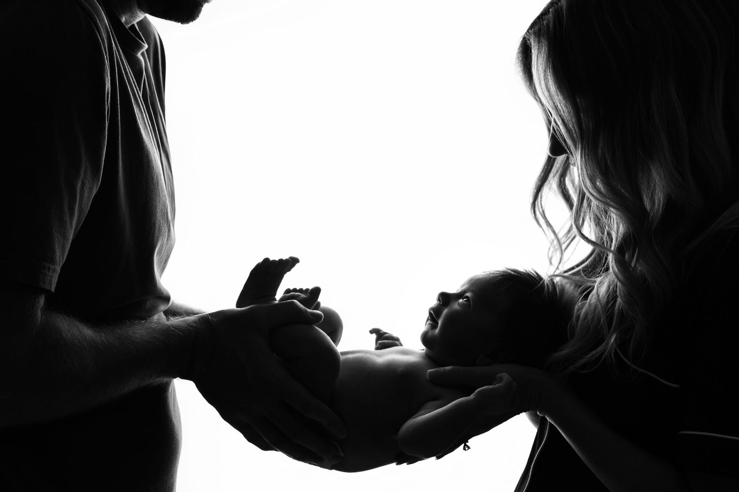 Backlit black and white portrait of parents holding newborn baby smiling up at them