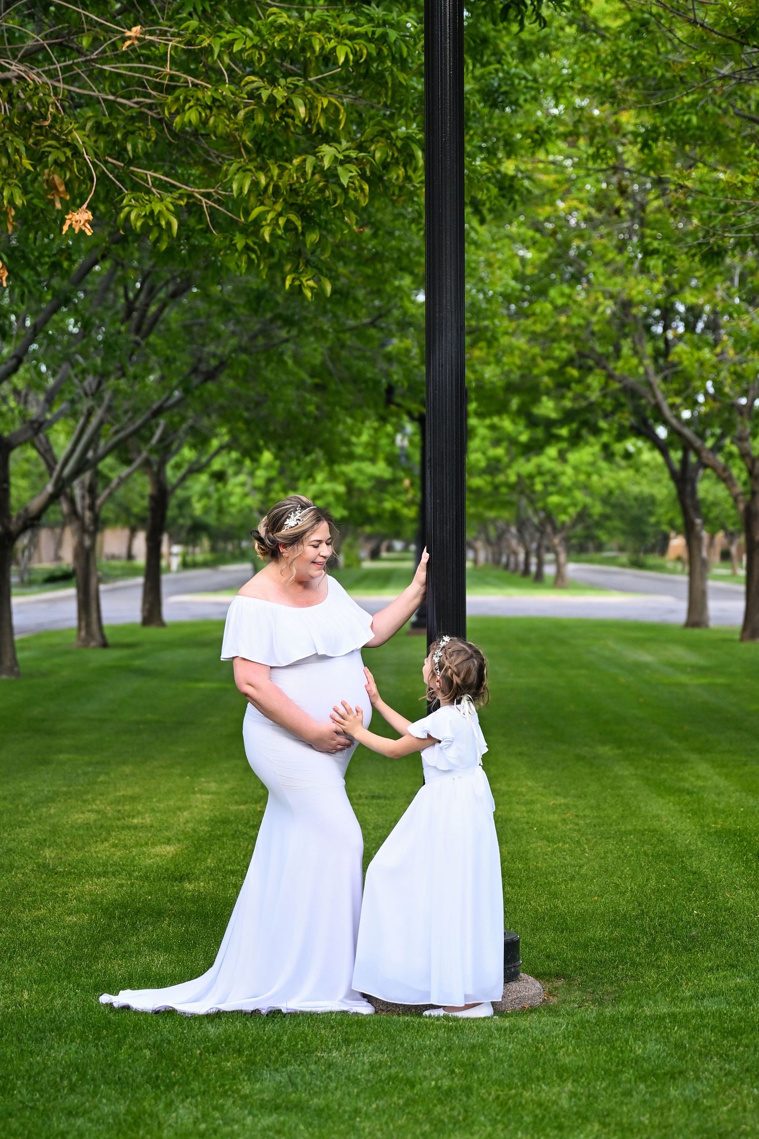 Woman looking down at her baby bump and older daughter in an open Scottsdale park.