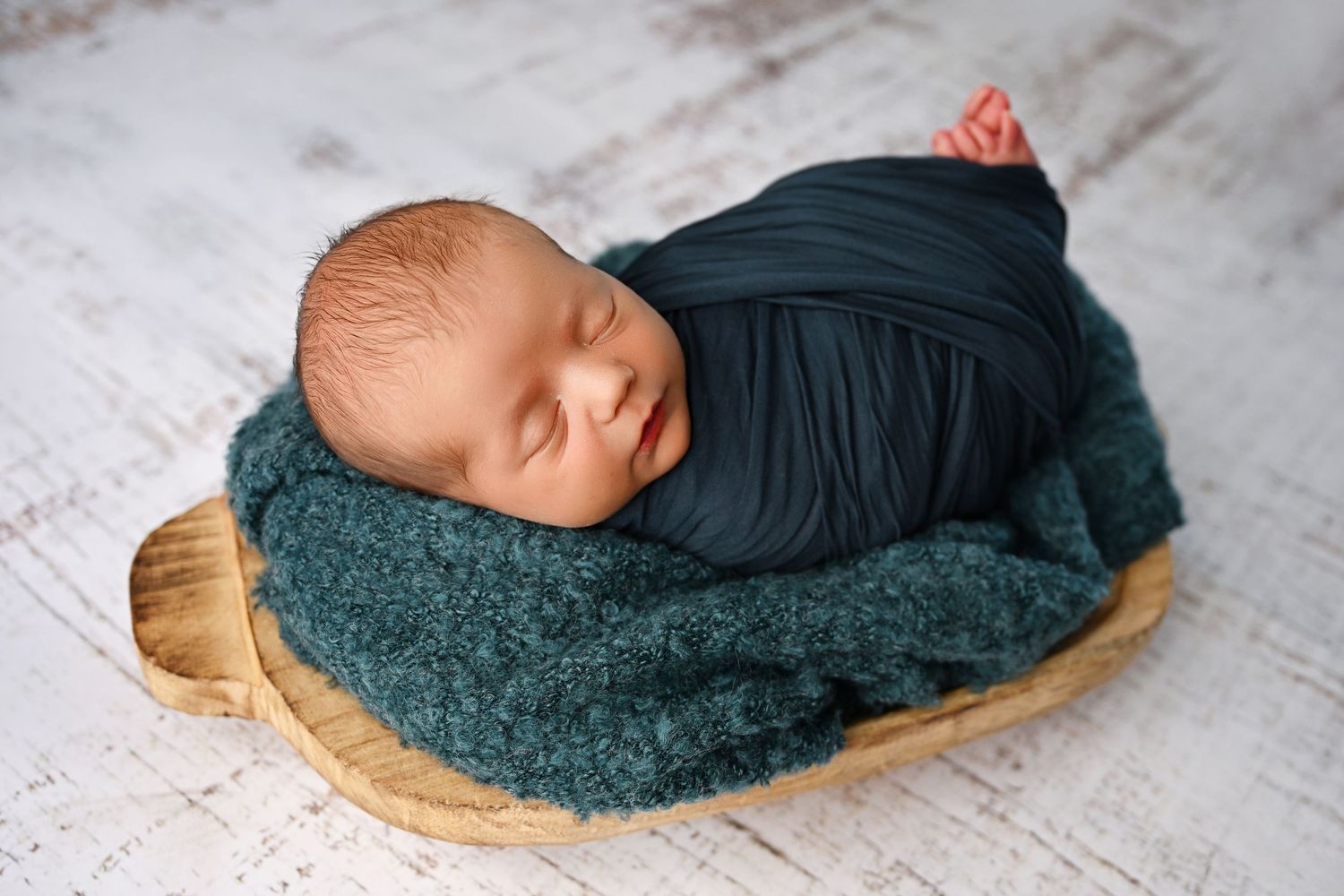 newborn baby boy swaddled in a peacock color laying down with toes out.