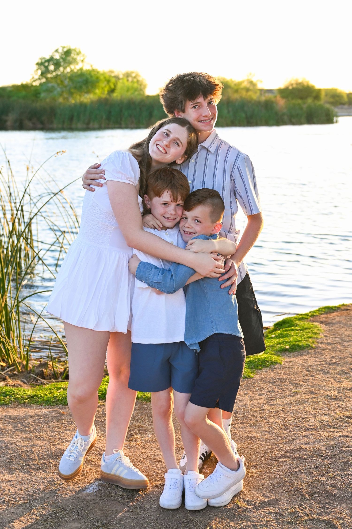 Siblings hugging and laughing towards the camera with wide smiles.