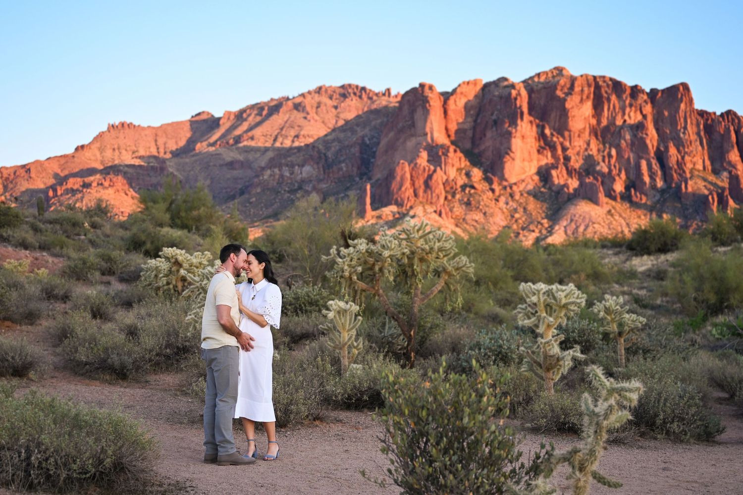 Couple snuggling in gorgeous Superstition Mountain Apache Junction Arizona Maternity photo. Husband holding wives belly