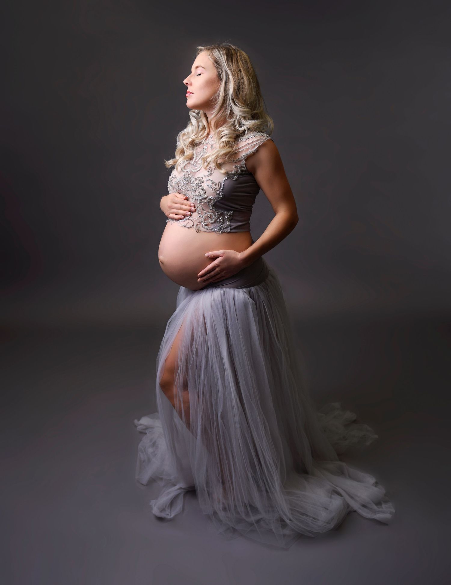 Elegant studio maternity portrait of a woman in a flowing gown with soft lighting.