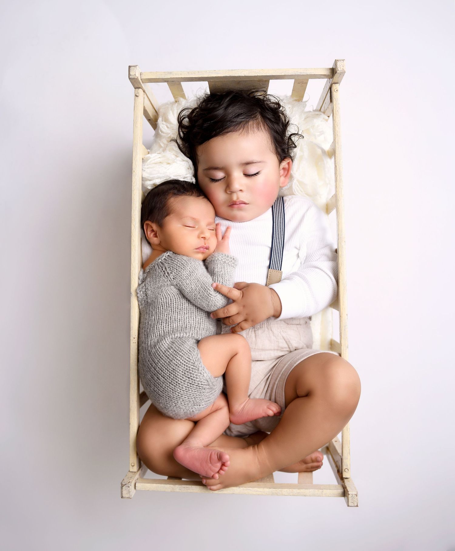Newborn baby and big brother sleeping together in a small crib taken a newborn photography studio
