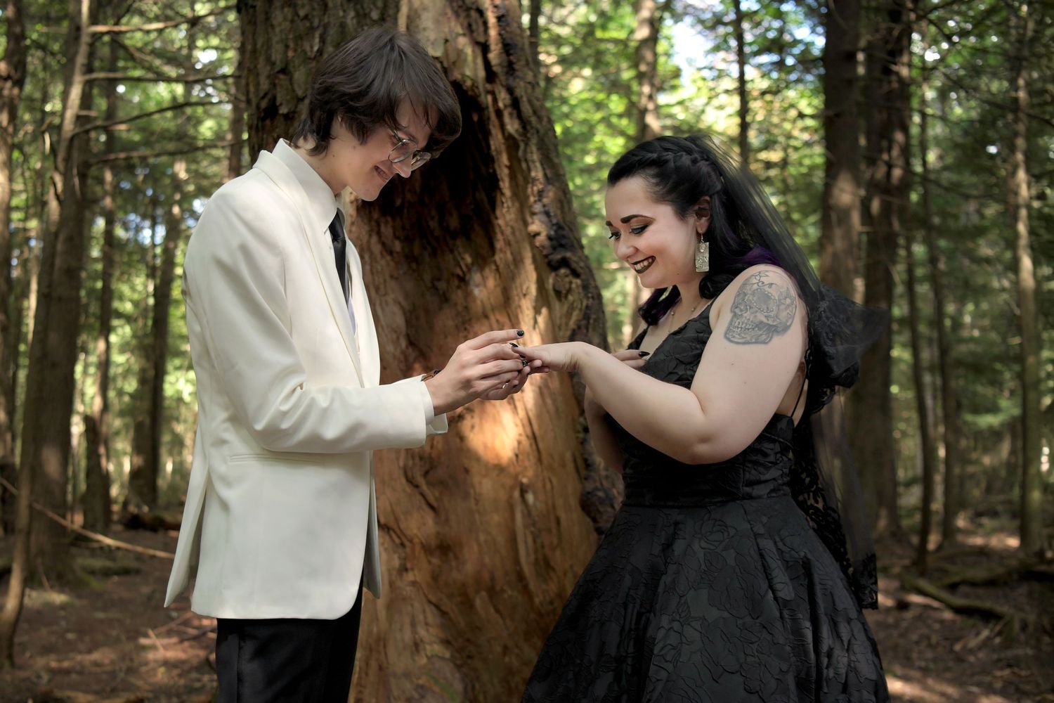 Wedding photo of groom putting ring on brides finger. Black wedding dress in the Northern Arizona woods.